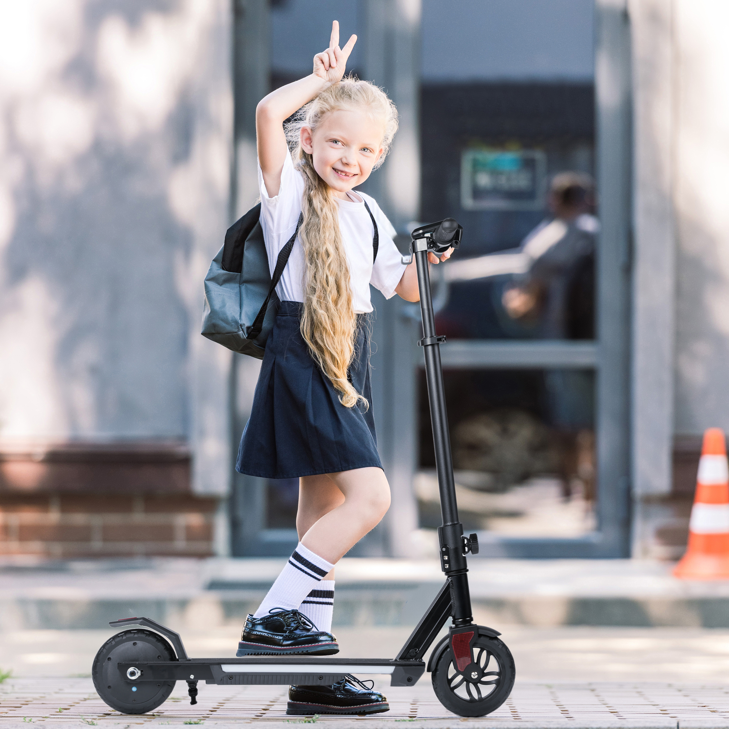 Ein blondes Mädchen mit Rucksack und Roller macht Friedenszeichen vor einem Gebäude.