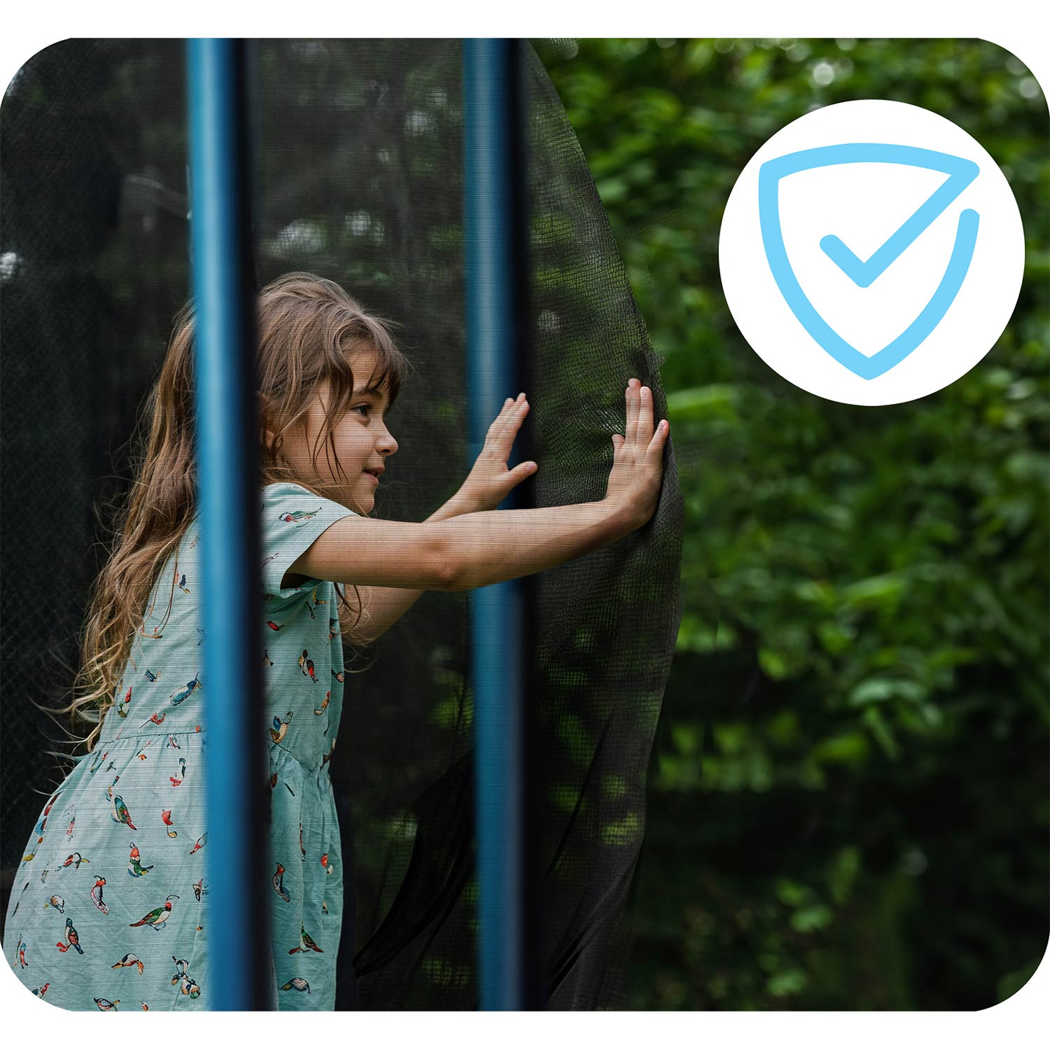 Mała dziewczynka w sukience w ptaki dotyka siatki zabezpieczającej trampoliny.