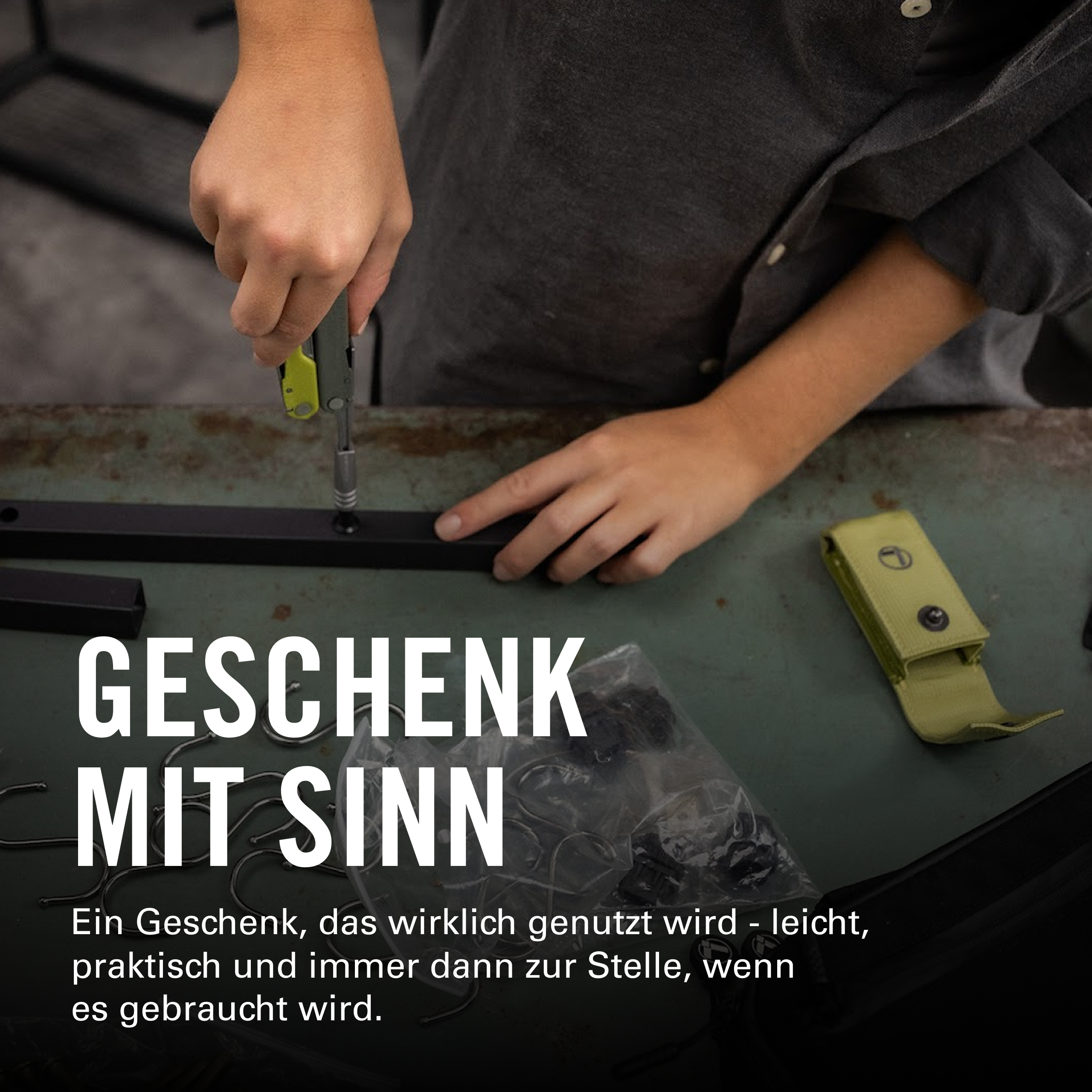 Eine Person schraubt mit einem Werkzeug an einem schwarzen Gestell. Text: Geschenk mit Sinn.