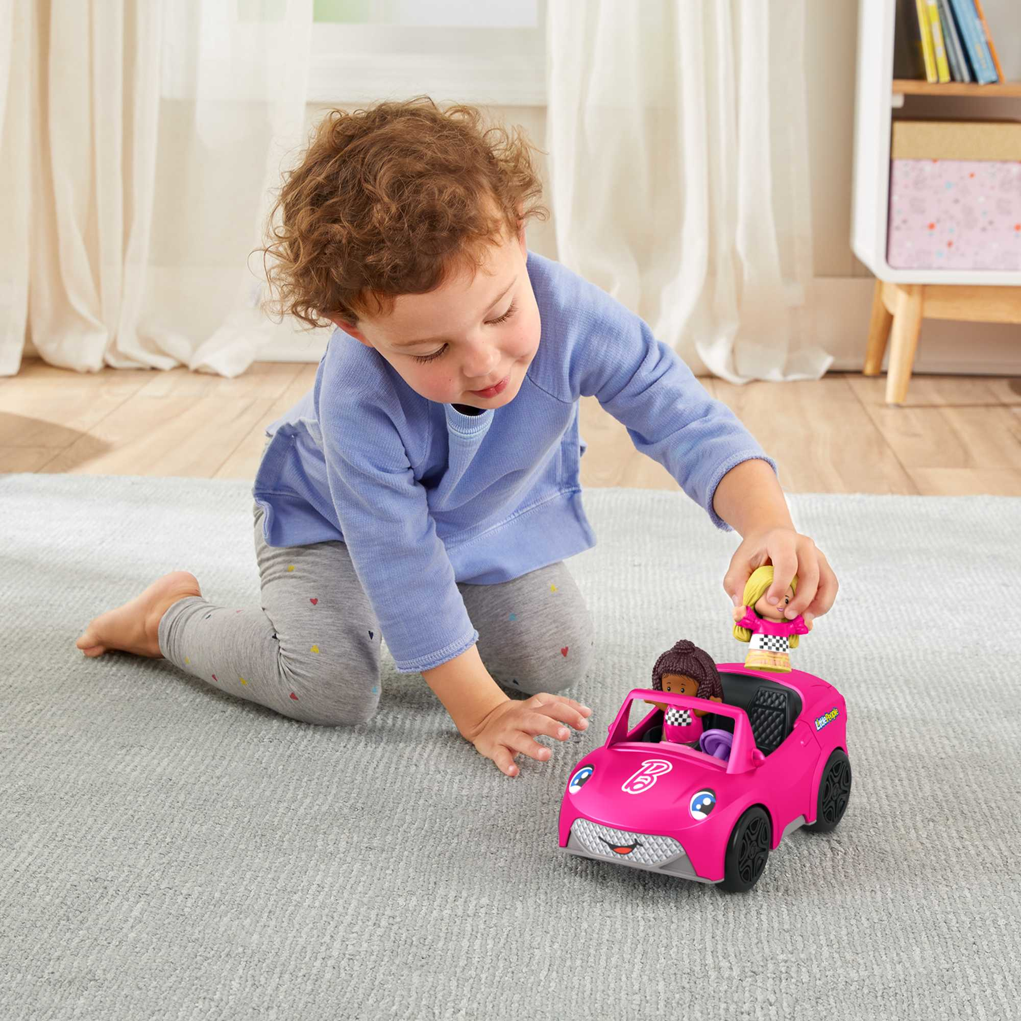 Un niño pequeño juega con un coche de juguete rosa con dos figuras.