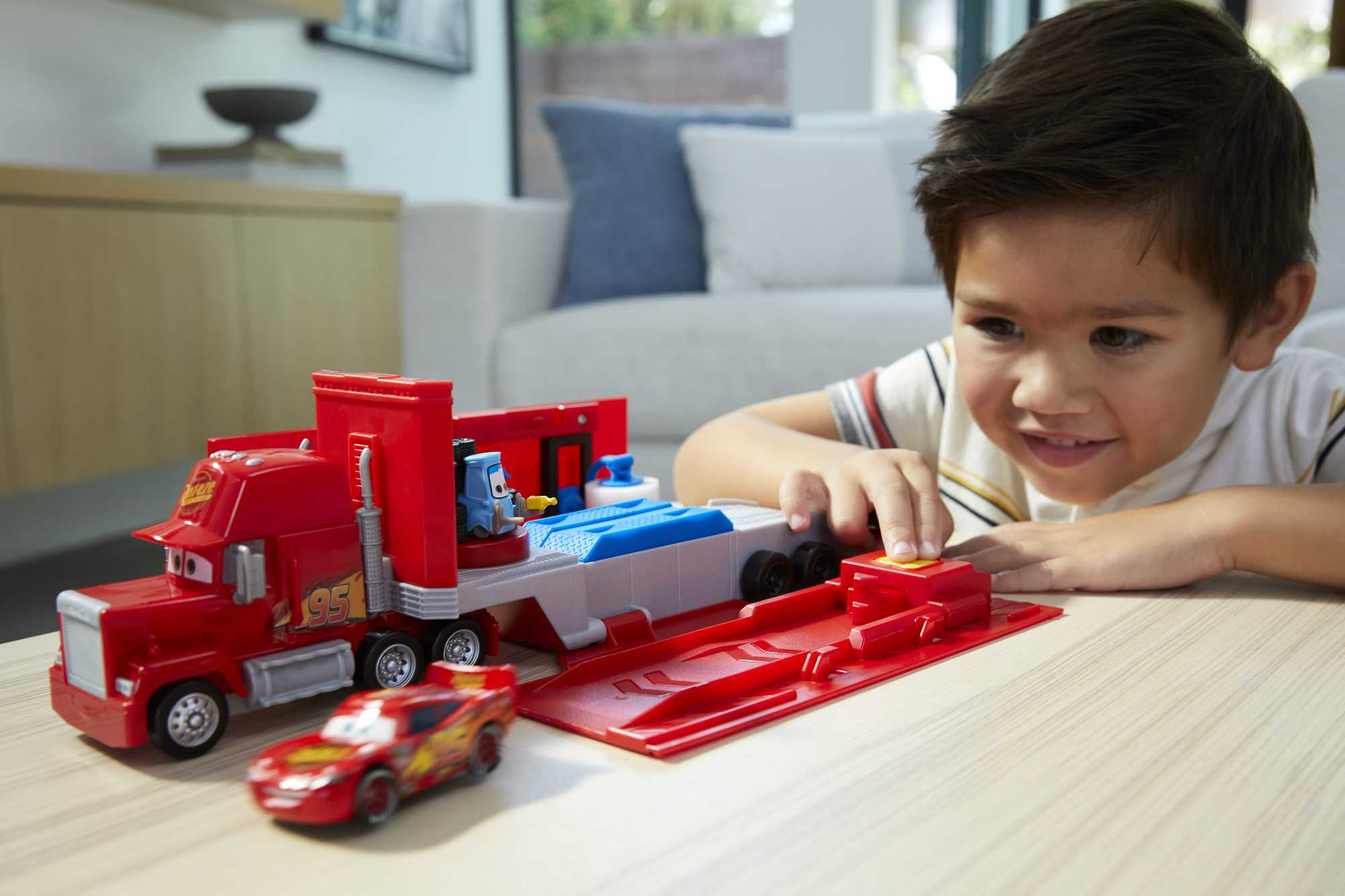A boy plays with a red toy truck and a small red race car.