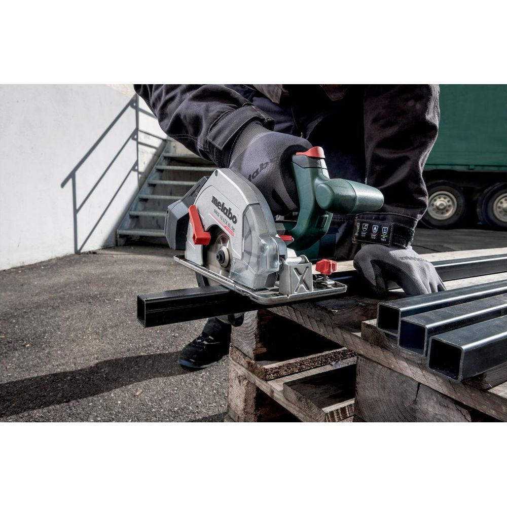 Eine Person mit Handschuhen schneidet mit einer Kreissäge einen Metallstab auf einer Palette.