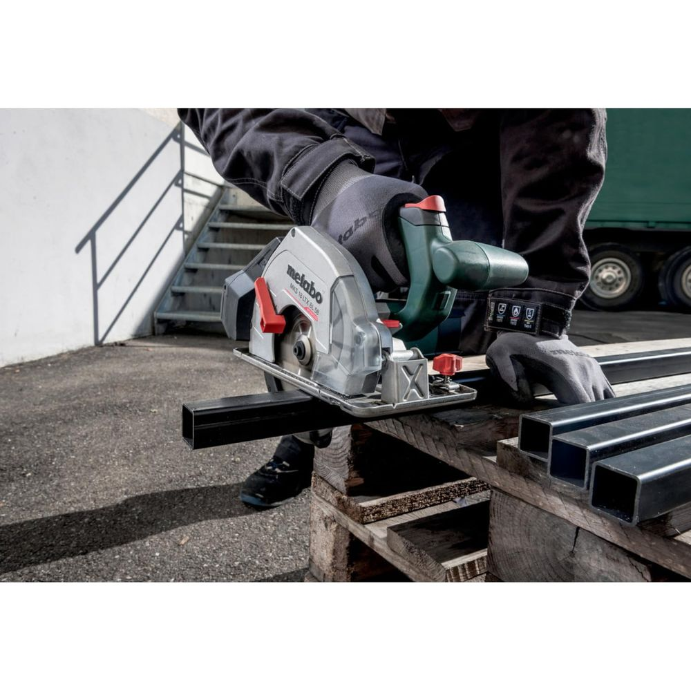 Kreissäge schneidet Metallrohr auf Holzpaletten, mit Mann in Arbeitskleidung.