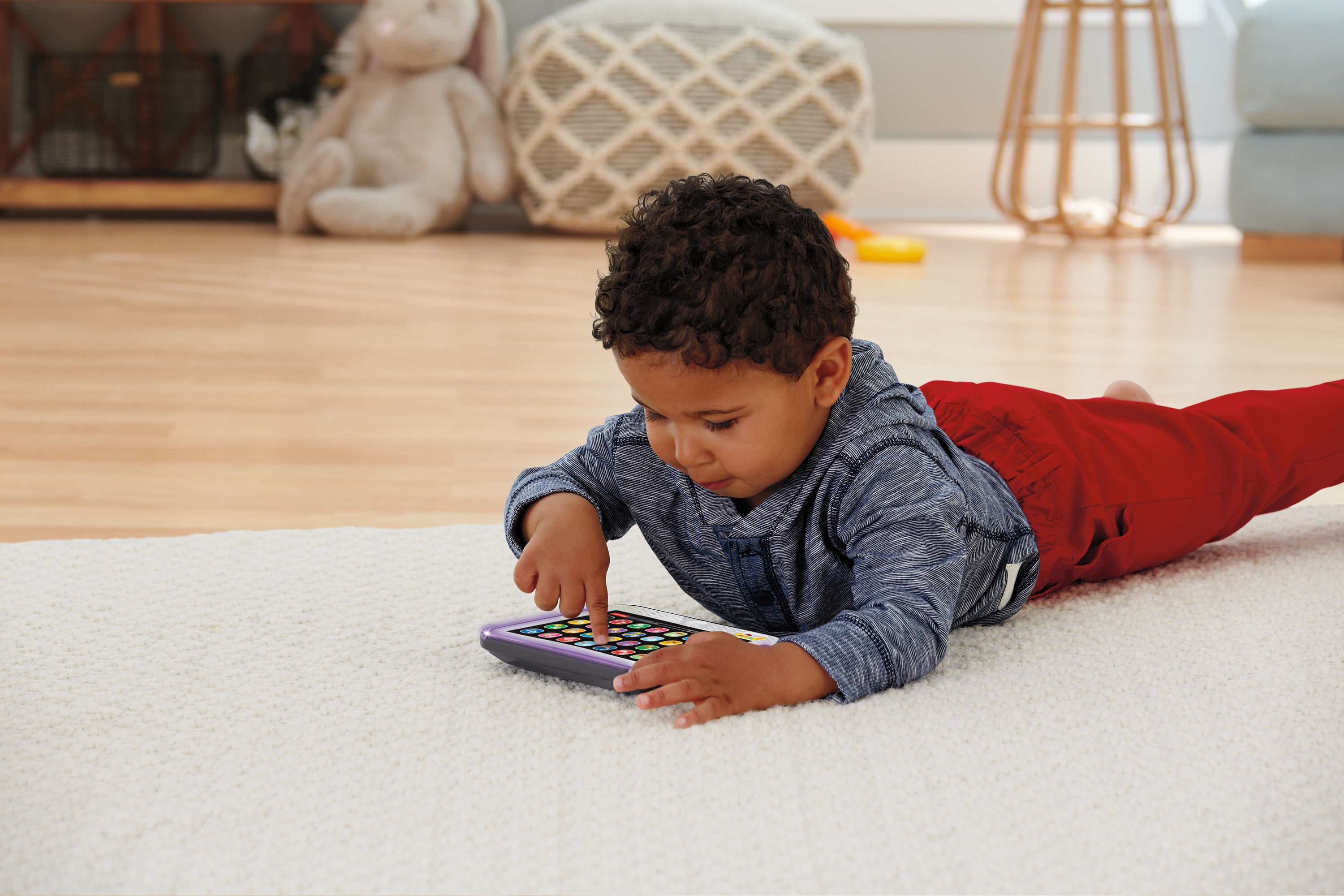 Un jeune garçon est allongé sur un tapis, jouant avec une tablette jouet colorée.