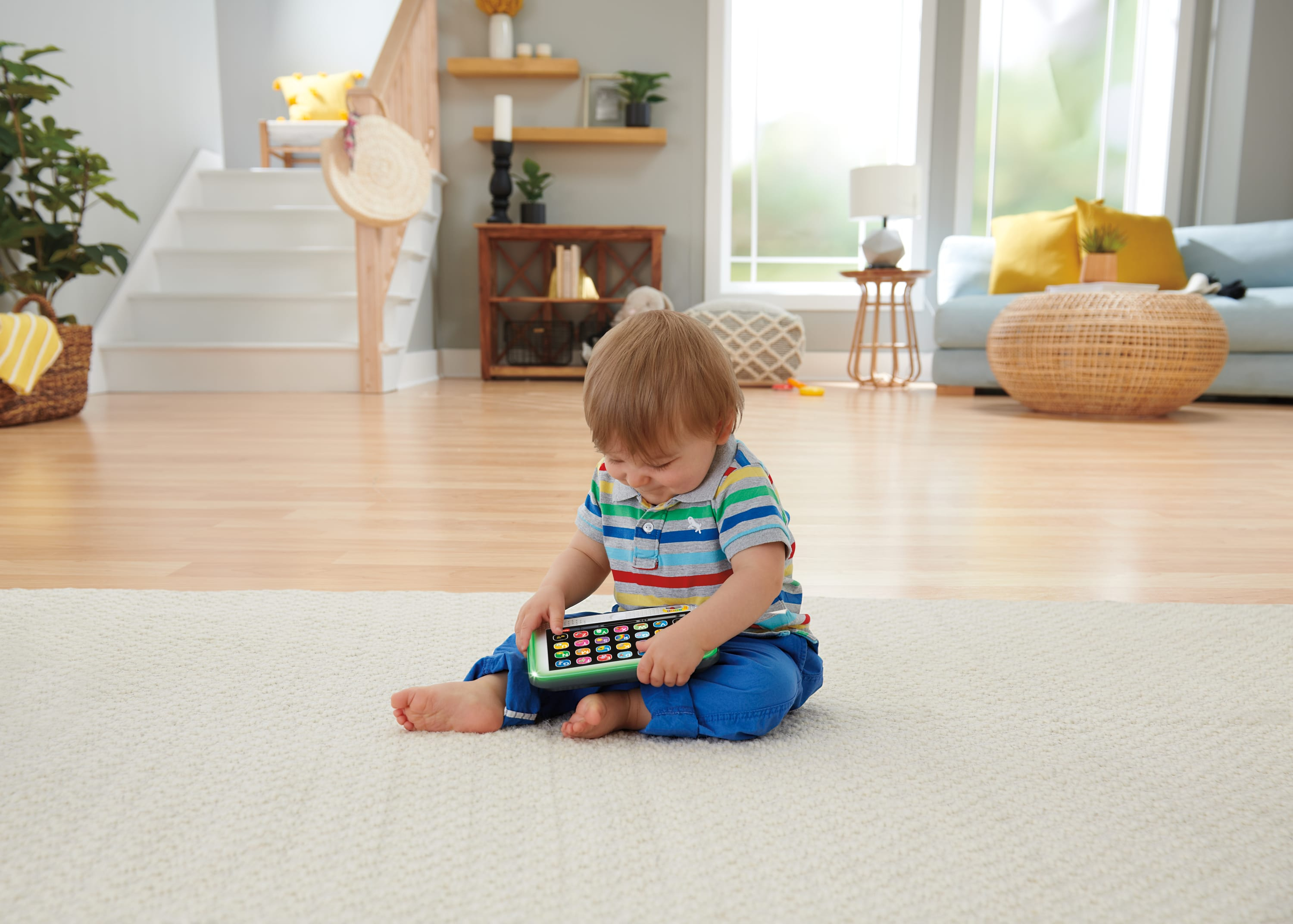Un tout-petit en chemise rayée colorée joue avec un téléphone jouet sur un tapis.