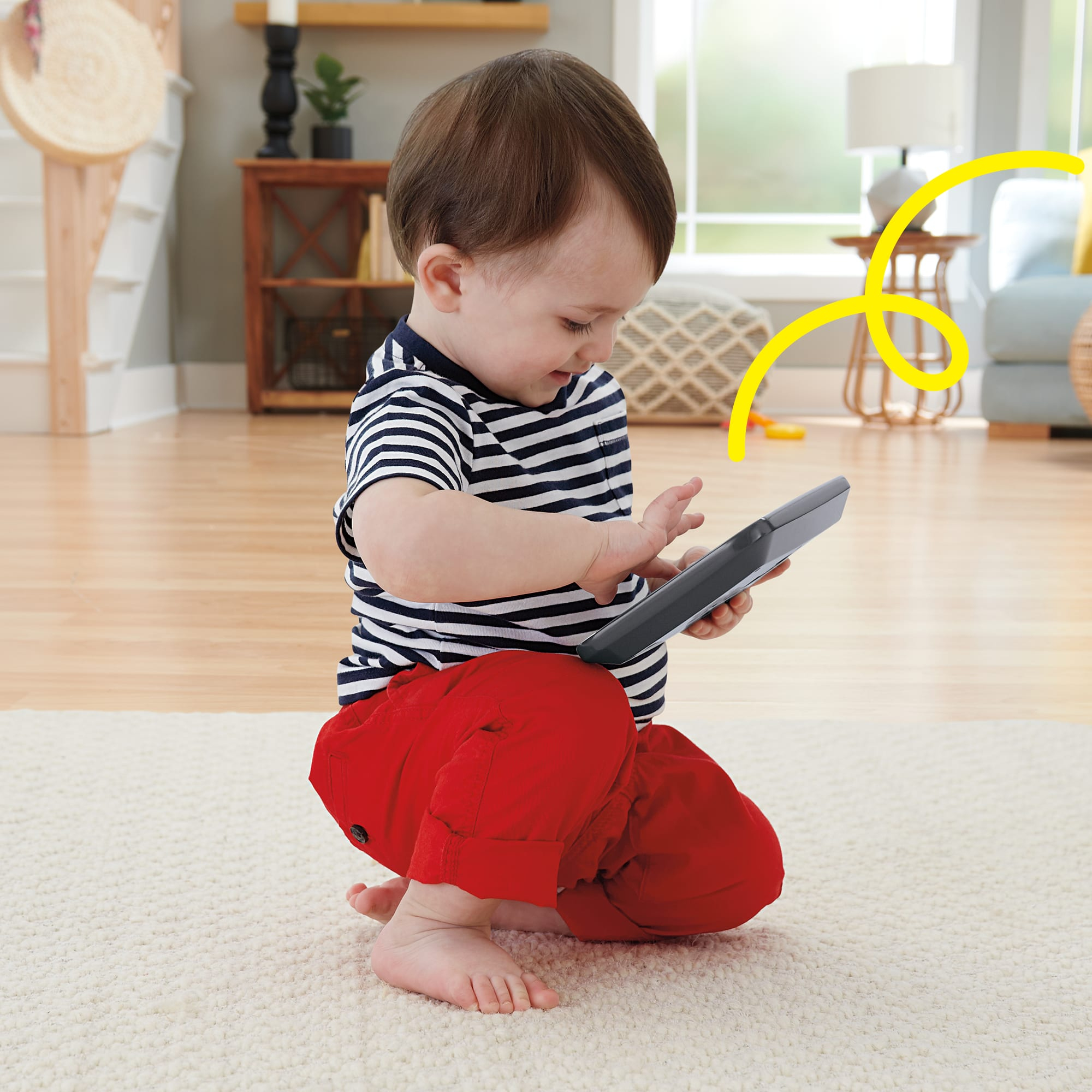 Un bébé en t-shirt rayé et pantalon rouge joue avec une télécommande sur un tapis.