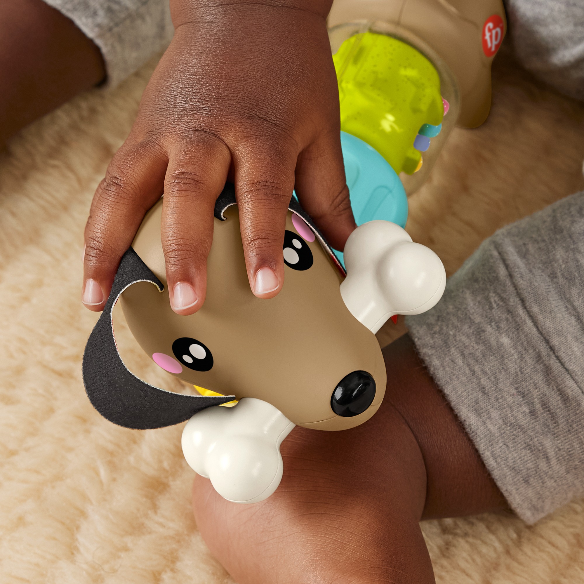 Ein Baby hält ein buntes Spielzeug in Form eines Hundes mit Knochen.