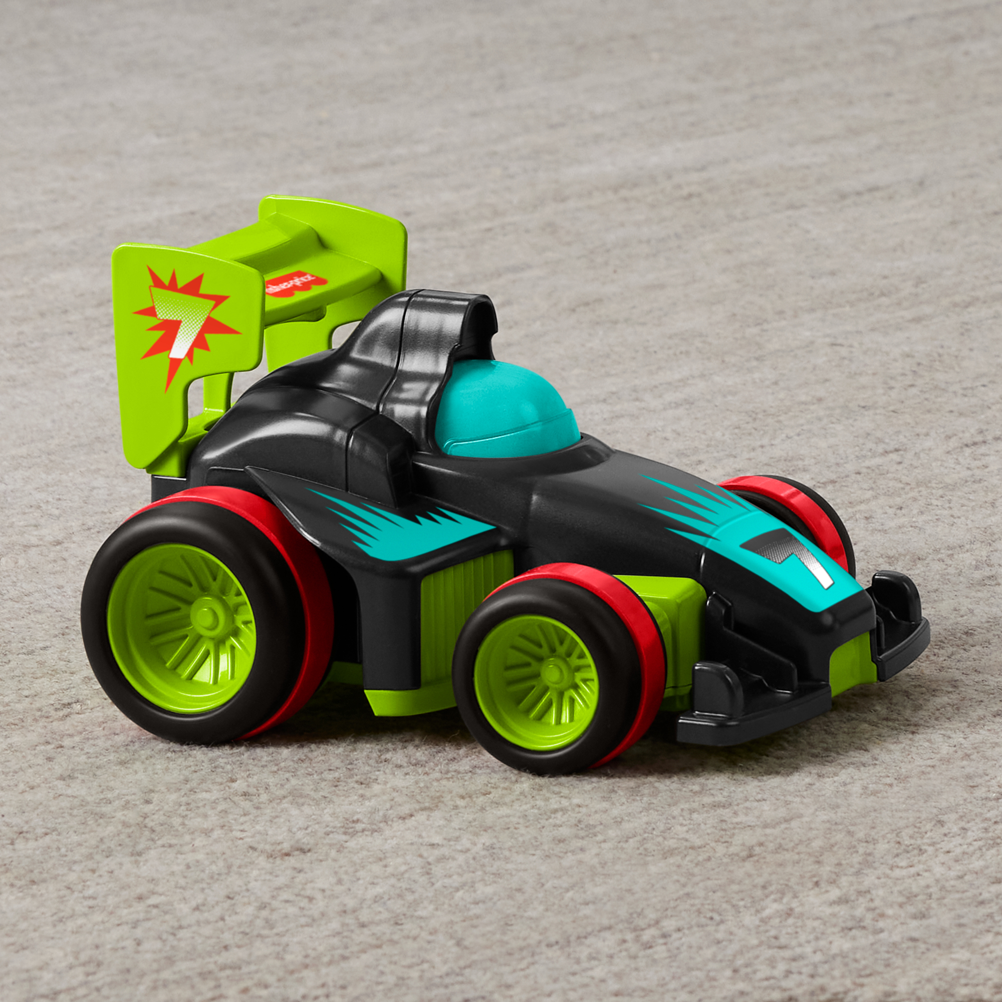 Un coche de carreras de juguete negro con ruedas verdes y alerón trasero sobre alfombra.