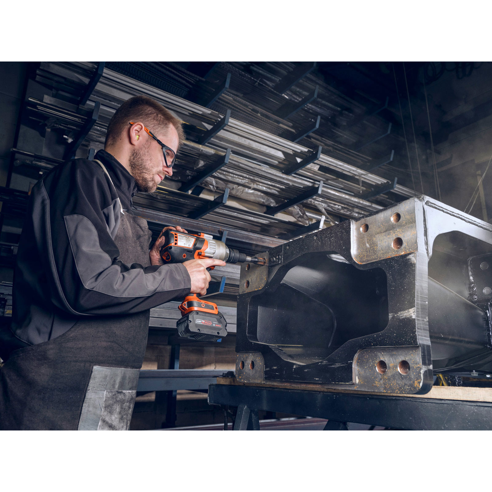 Ein Mann mit Schutzbrille benutzt einen Akkuschrauber an einem großen Metallteil.