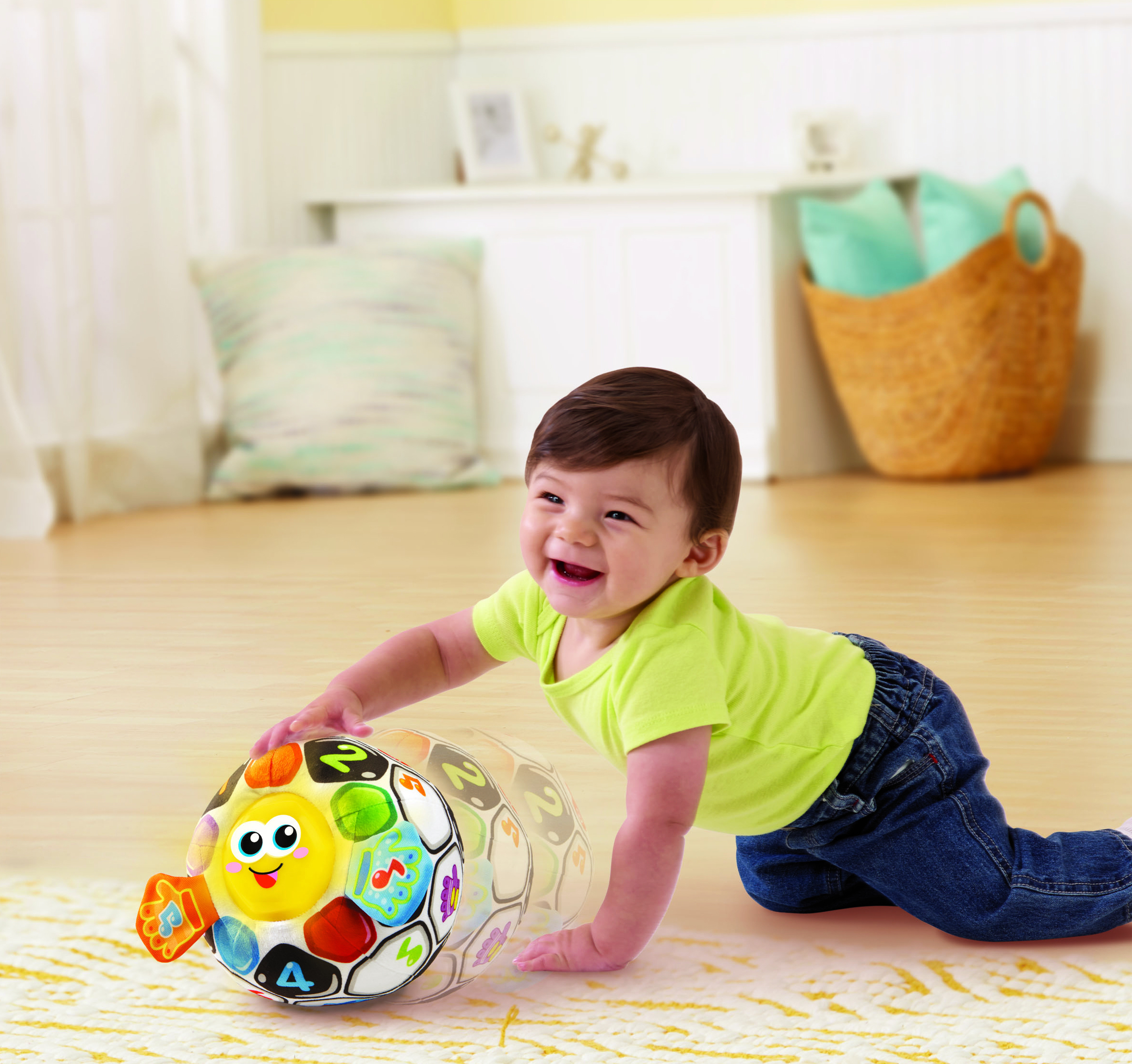 Ein Baby in einem lindgrünen Hemd und Jeans krabbelt auf einem hellen Holzboden, lacht und greift nach einem bunten Spielzeugball.