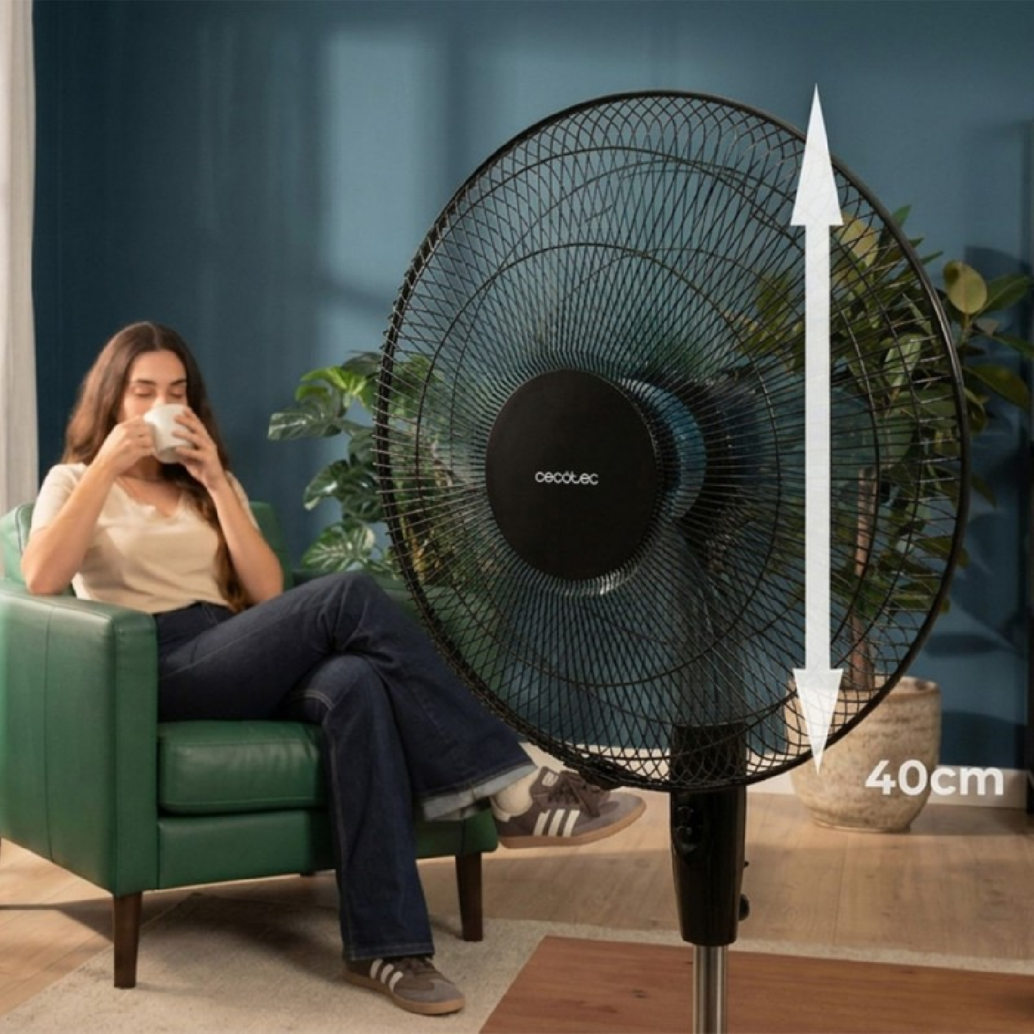 Una mujer bebe en un sillón junto a un ventilador de 40cm de diámetro.