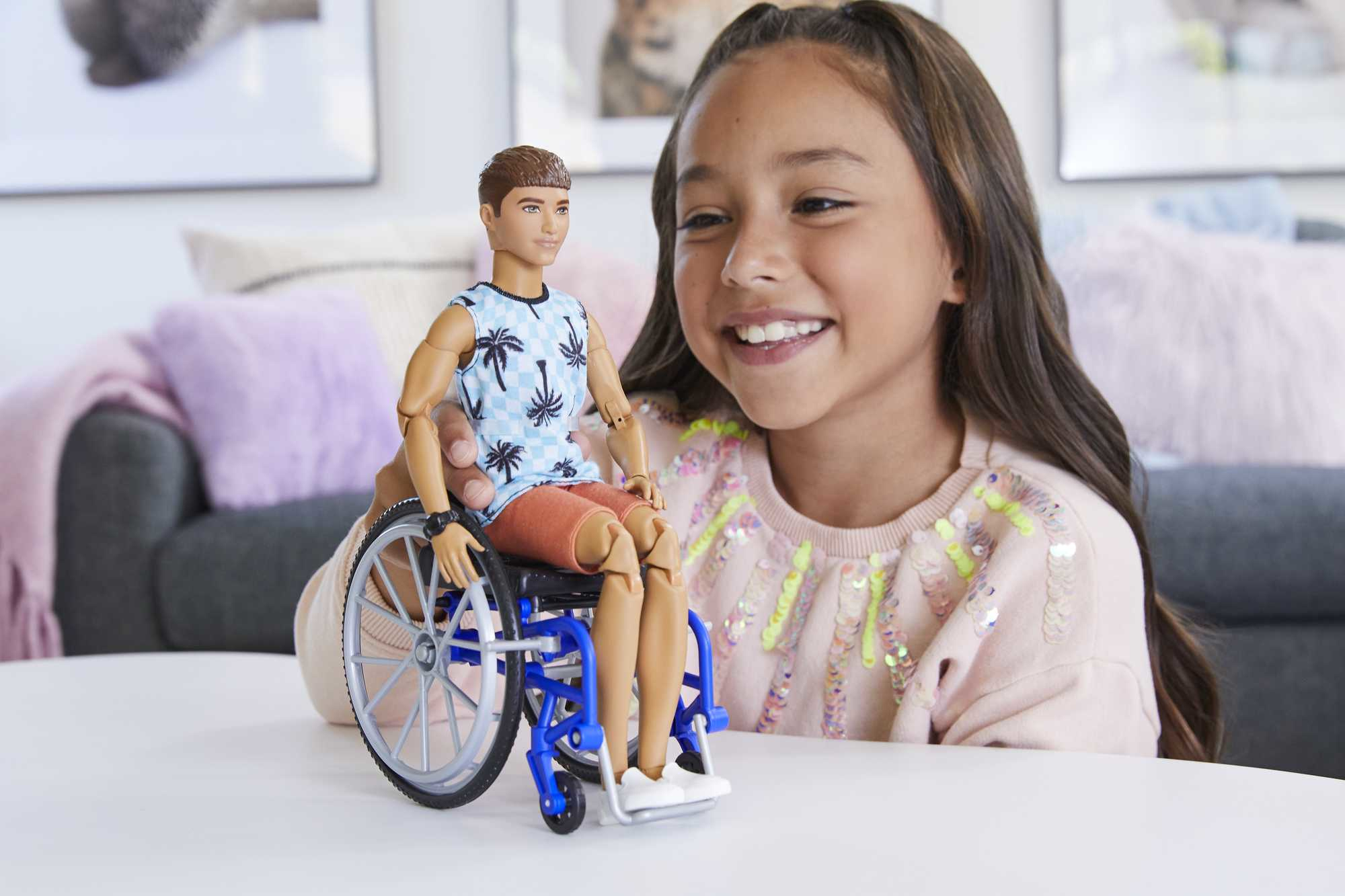 Ein Mädchen lächelt und hält einen Ken-Doll in einem Rollstuhl.