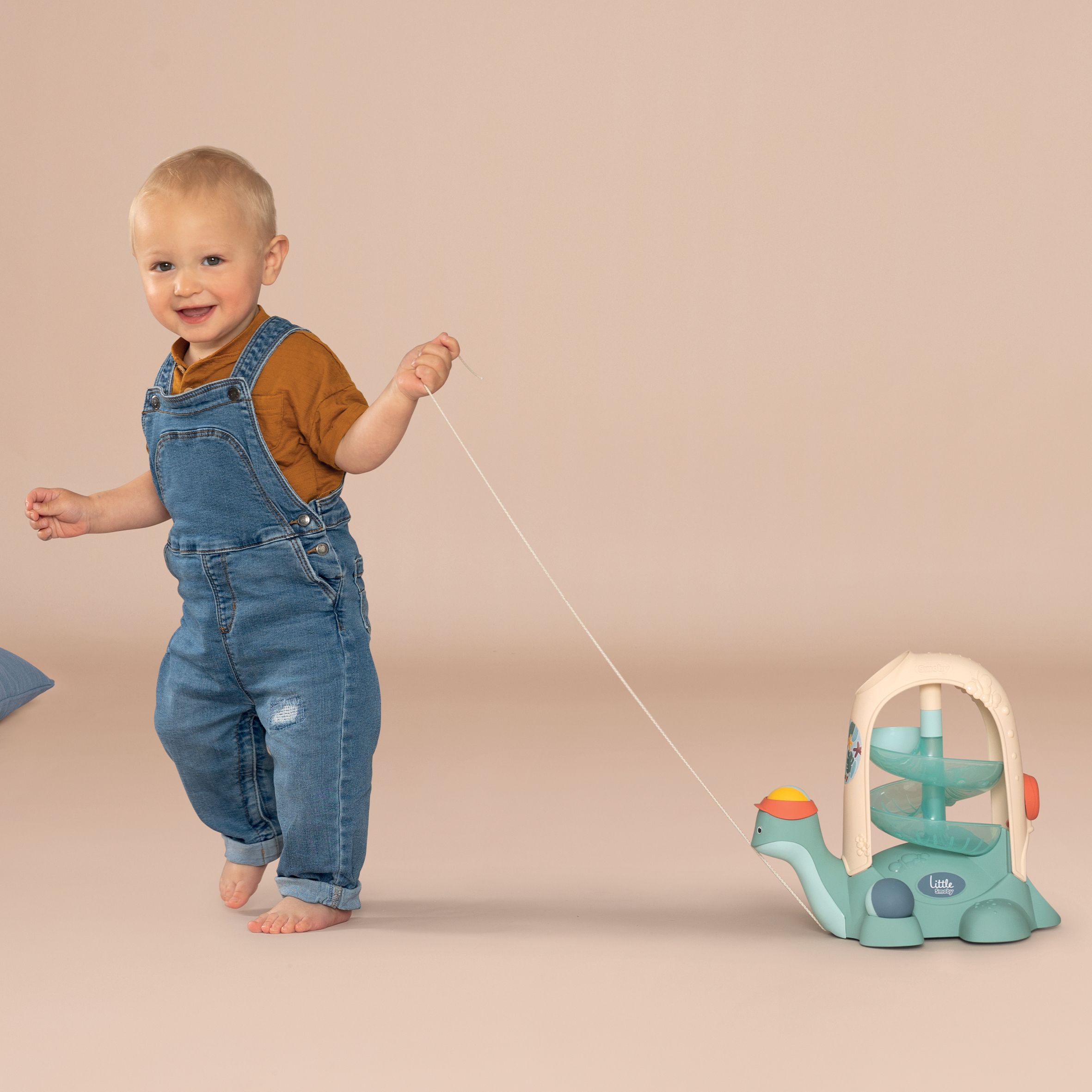 Un bimbo in salopette di jeans tira un giocattolo tartaruga con un filo.