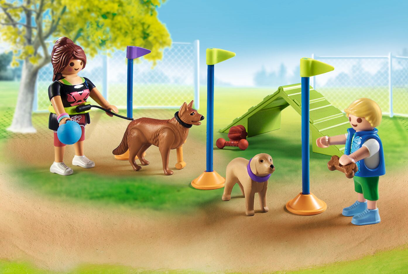 Dos niños entrenan perros en un patio de recreo con equipo de agilidad y banderas.