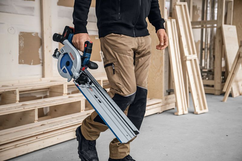 Mann mit blauer Kreissäge und Führungsschiene in Werkstatt mit Holz.