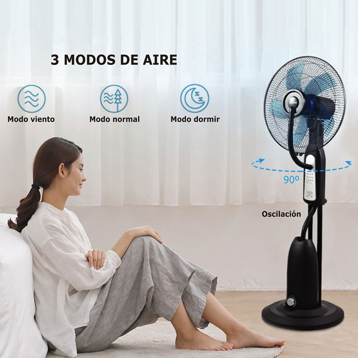Una mujer sentada en el suelo frente a un ventilador con 3 modos de aire.