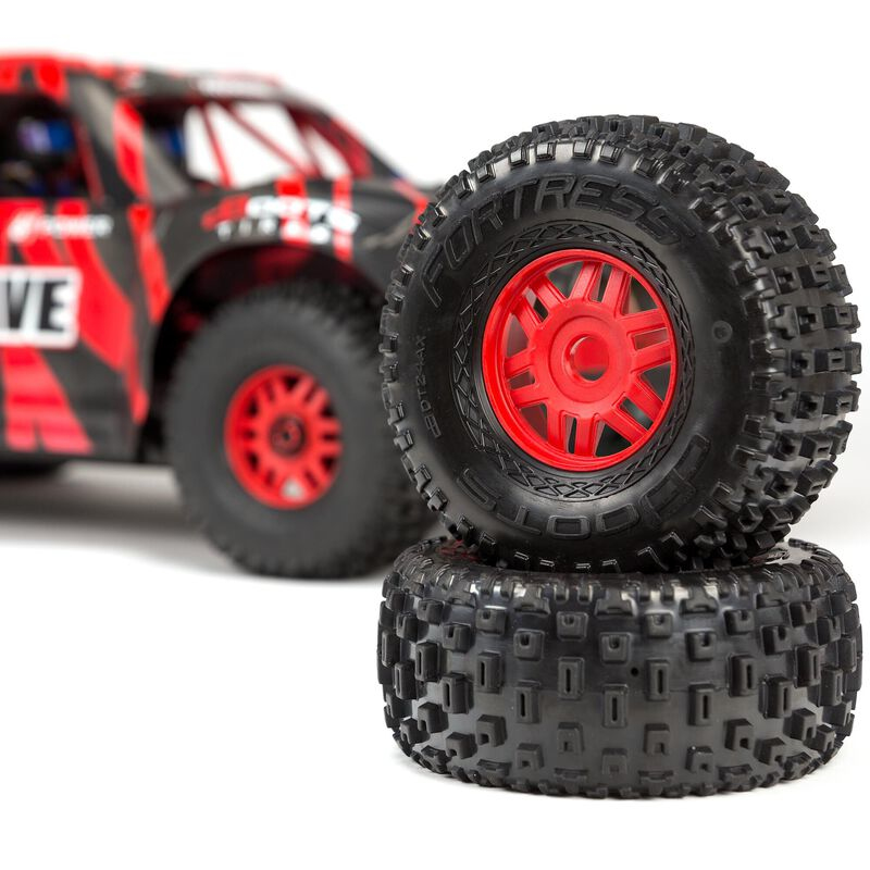 Deux pneus de voiture RC noirs à jantes rouges empilés. Une voiture RC rouge et noire floue à l'arrière.
