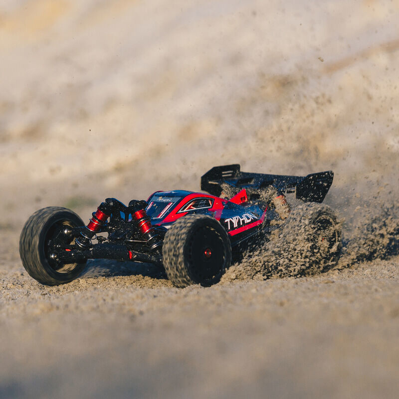 Un coche RC rojo y negro avanza rápido por la arena, levantándola.