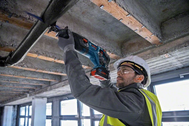 Mann mit Säge schneidet Rohr unter Beton. Gerüst und Fenster im Hintergrund.