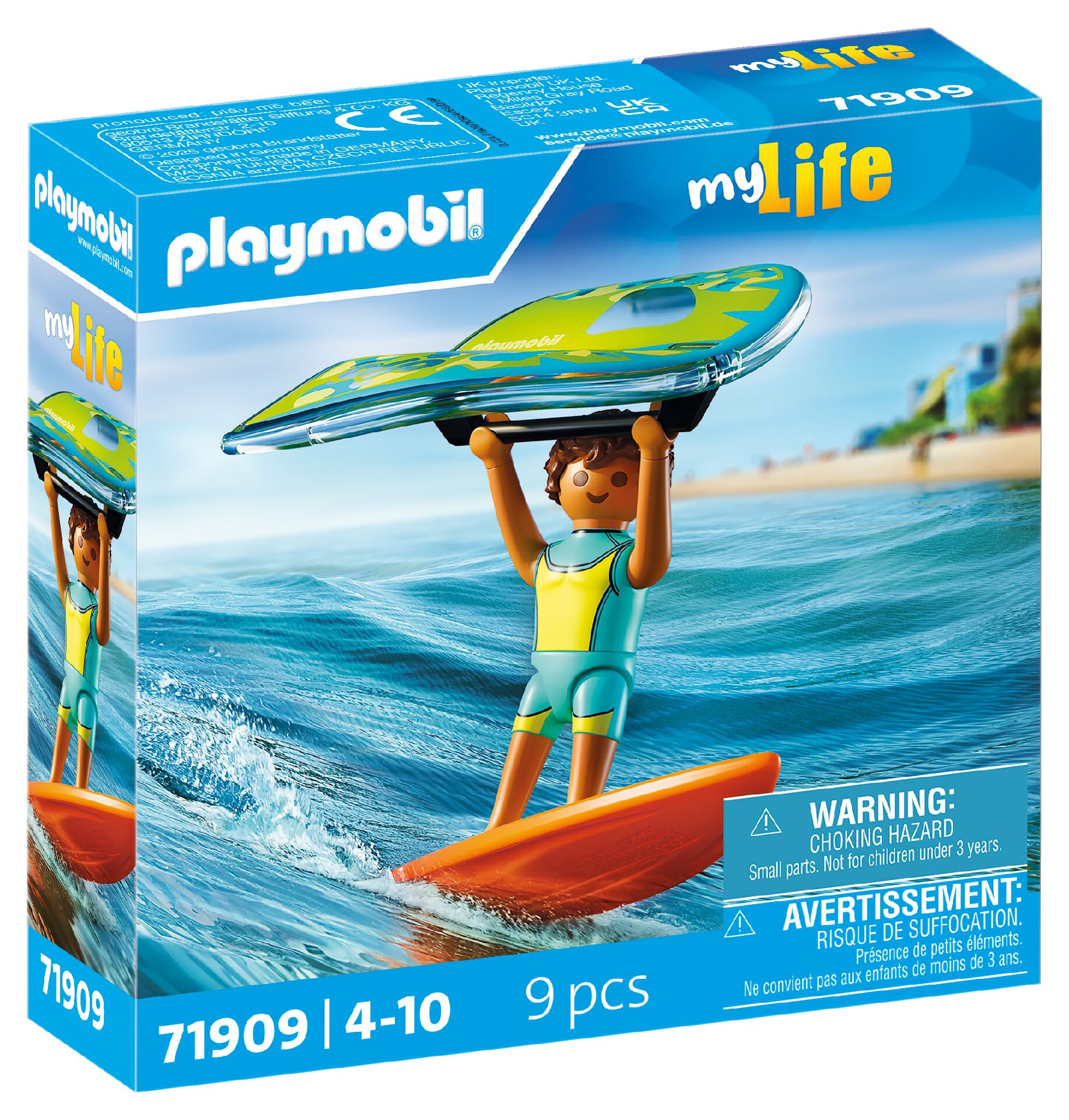 Caja de juguete Playmobil con un niño en traje de neopreno sosteniendo una tabla de surf sobre olas azules, con playa y ciudad de fondo.