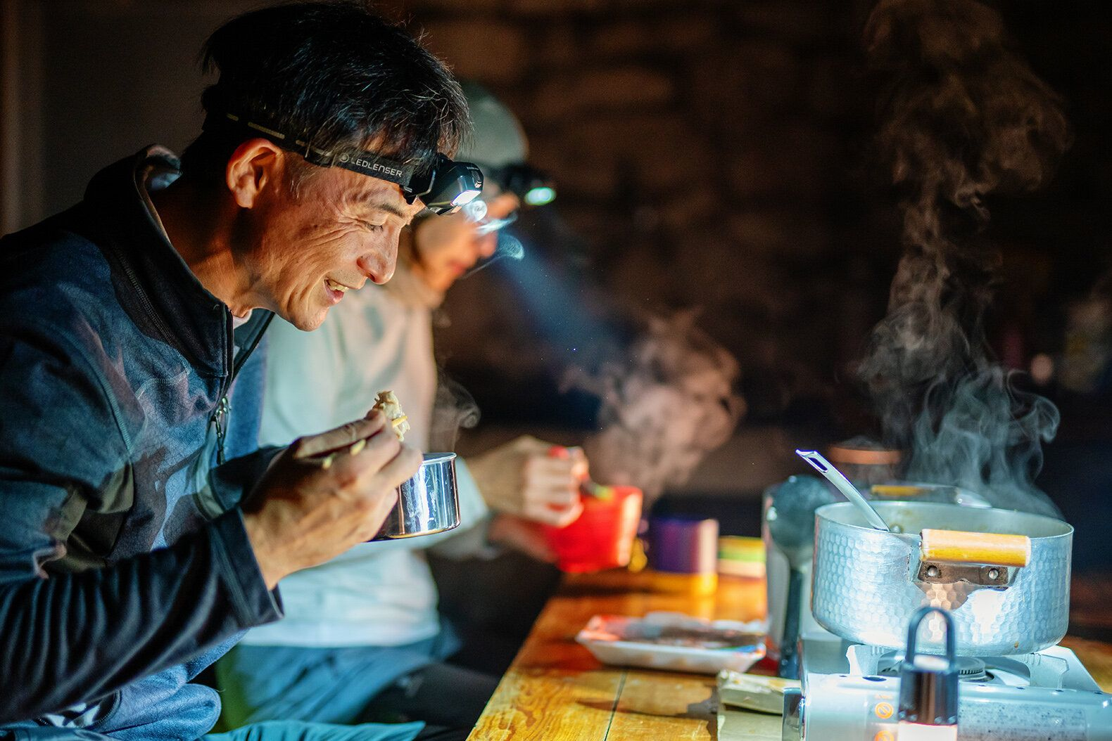 Männer mit Stirnlampen essen und kochen im Dunkeln.