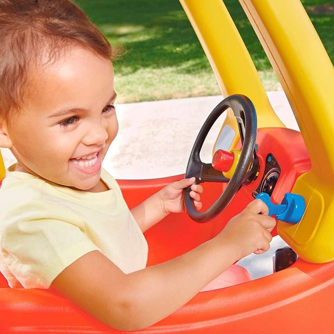 Una bambina siede in un'auto giocattolo rossa, tenendo il volante.