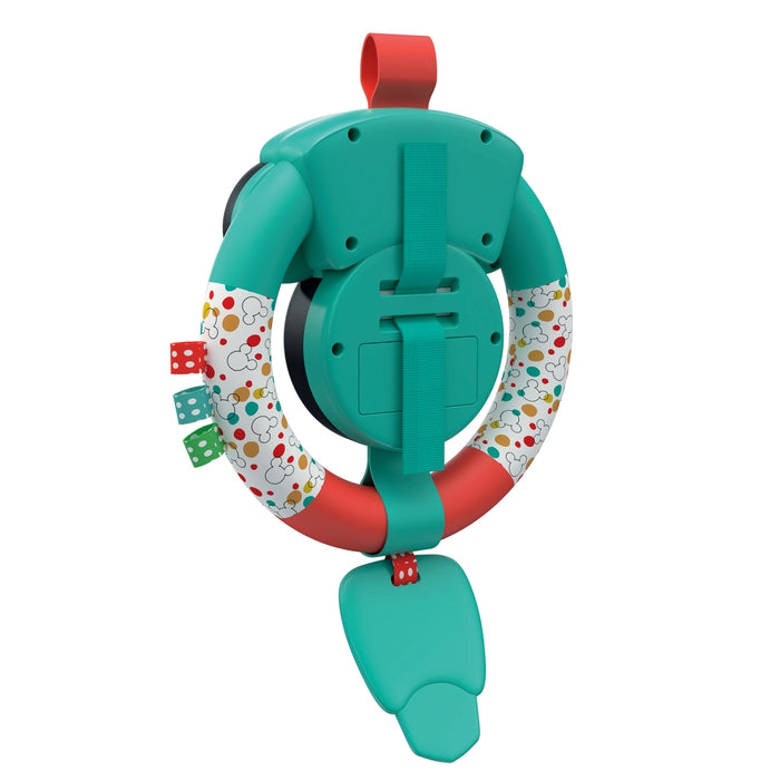 Un volante de juguete para bebé verde y rojo con patrones coloridos y juguetes colgantes en forma de dado sobre un fondo blanco.