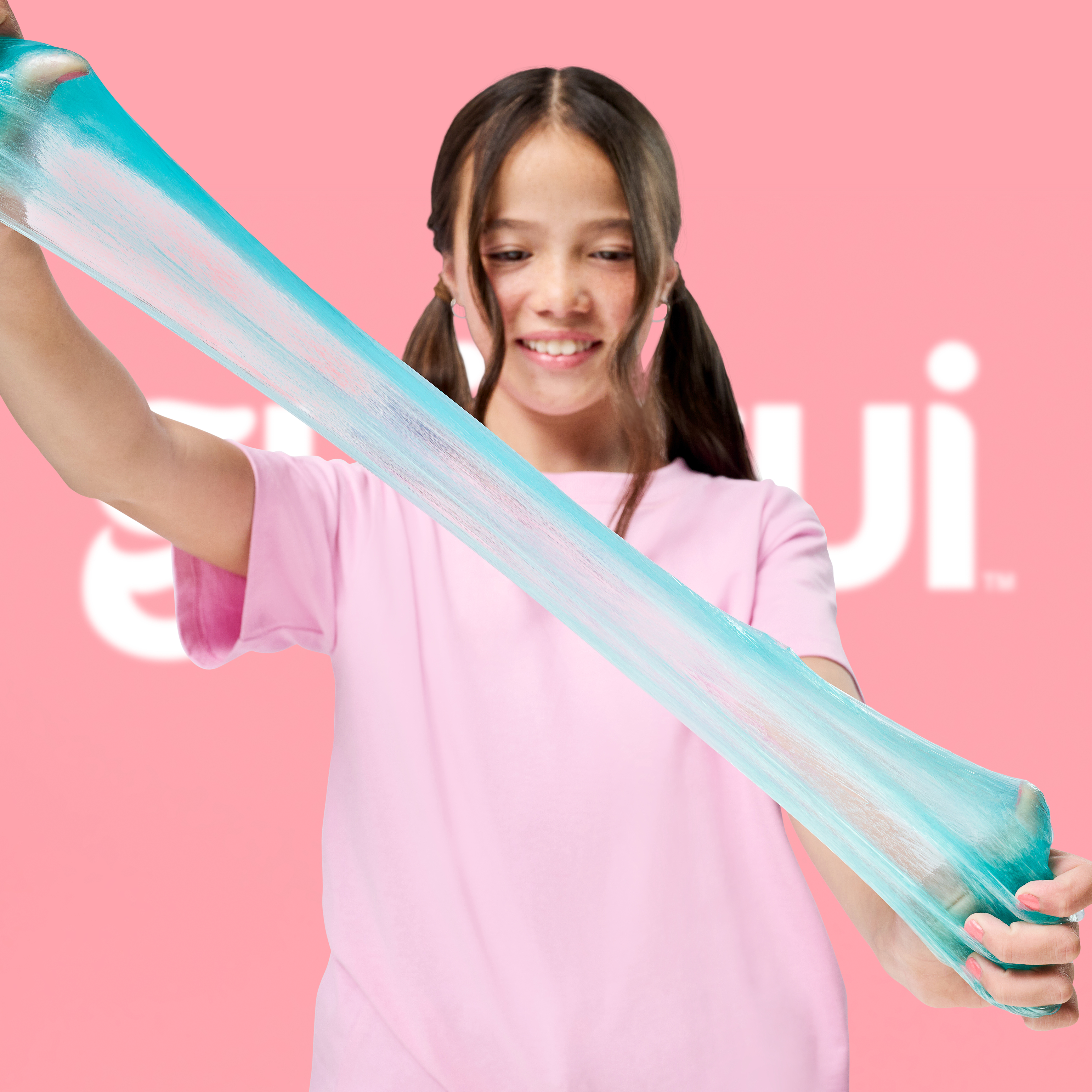 Una niña con coletas estira baba turquesa con sus manos.