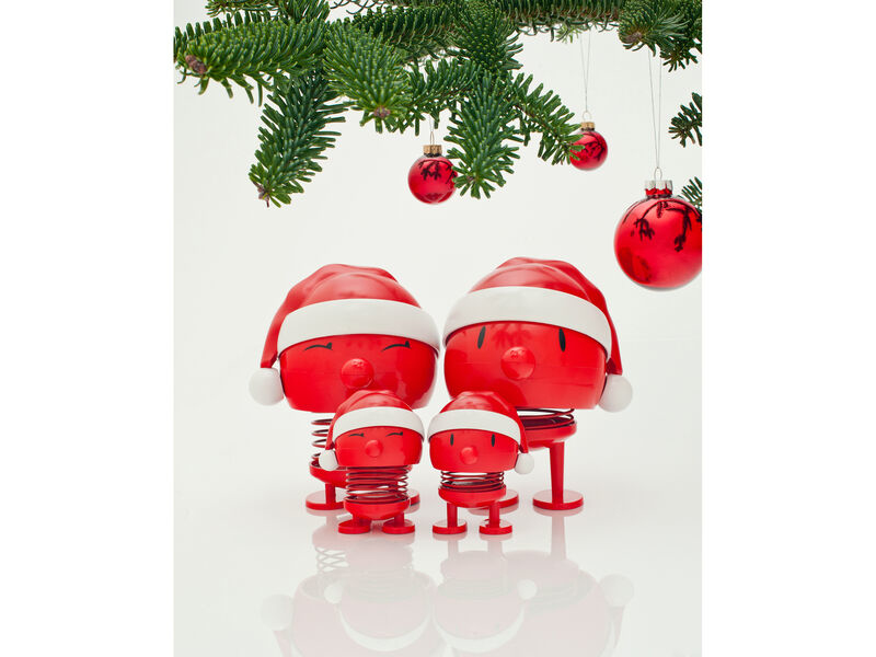 Quattro figure rosse con cappelli di Babbo Natale sotto un albero di Natale con ornamenti.