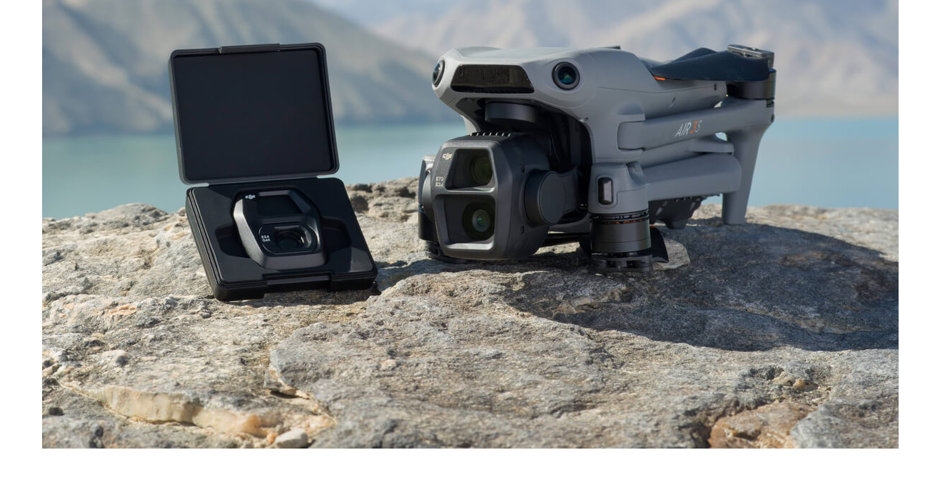 Grauer DJI Air 3 Drohne neben schwarzem Koffer mit Fernbedienung auf Felsen.