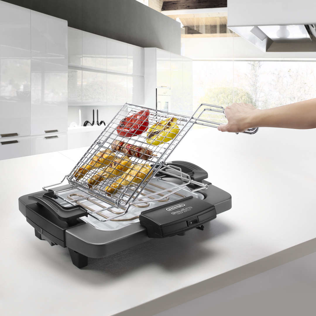 Una mano griglia spiedini di cibo e peperoni su una griglia elettrica in una cucina moderna.