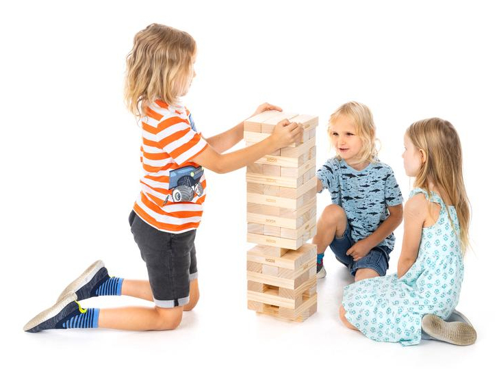 Tre bambini costruiscono una torre alta con blocchi di legno su sfondo bianco.