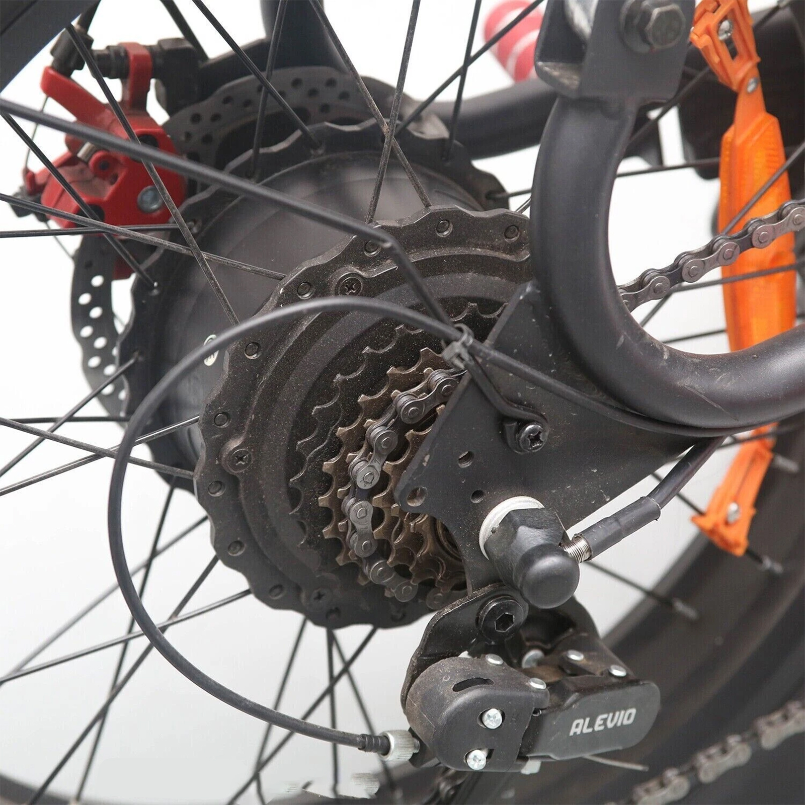 Primer plano del desviador trasero de una bicicleta con casete, cadena y freno rojo.