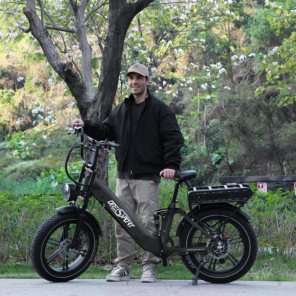 Mann mit schwarzem E-Bike im Freien neben einem Baum mit weißen Blüten.