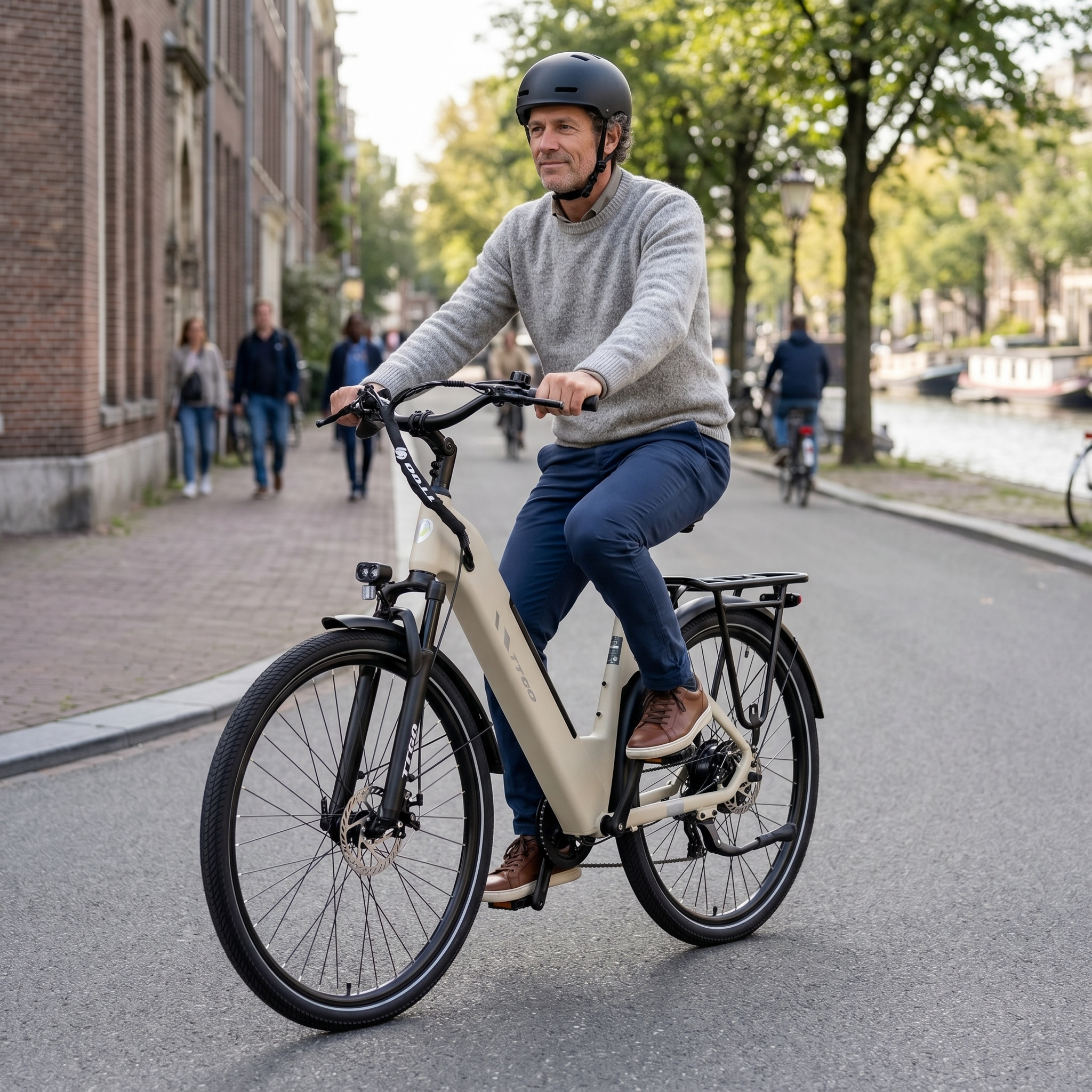 Mann im grauen Pullover und Helm fährt ein beiges E-Bike in einer Stadtstraße am Kanal.