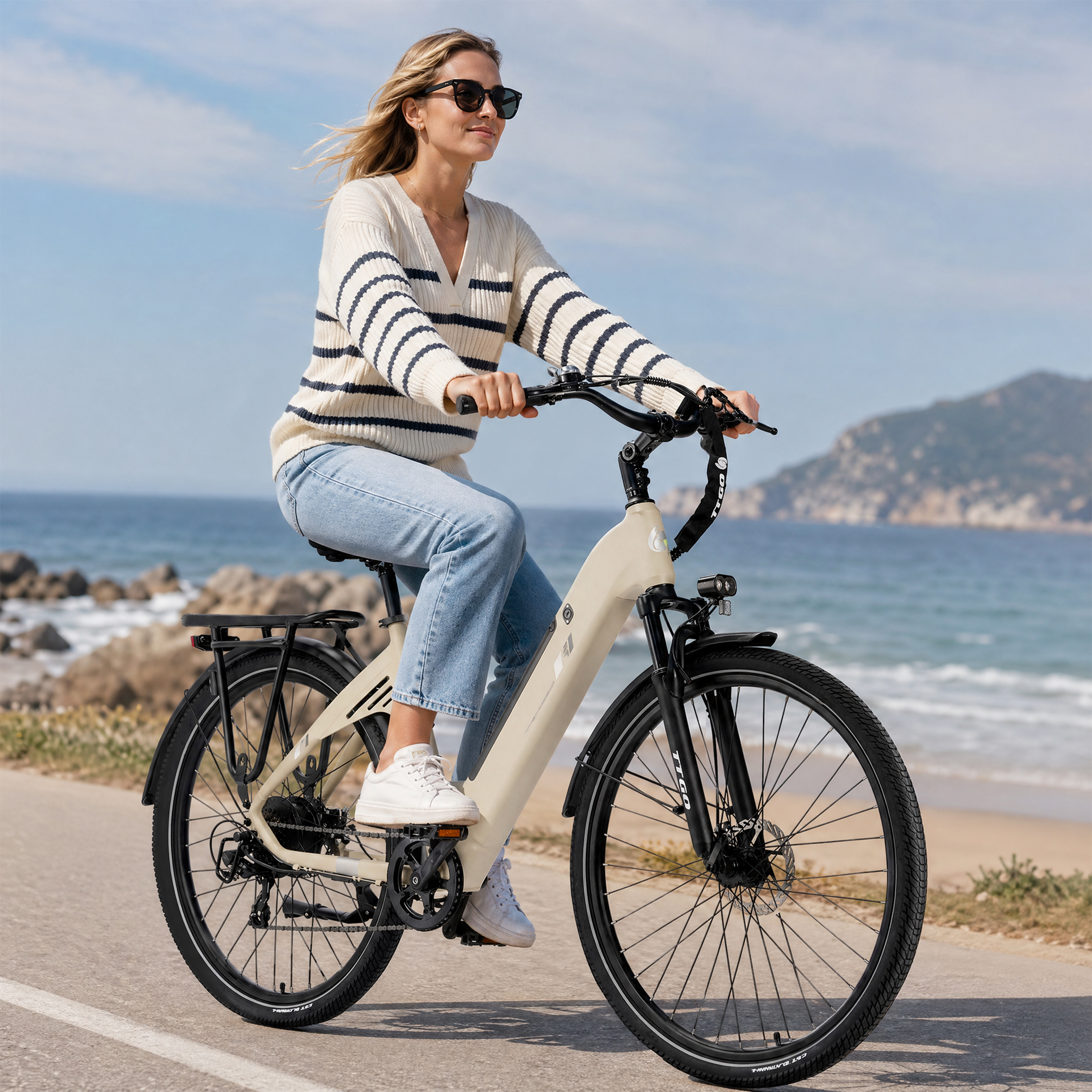Eine Frau fährt ein beiges Fahrrad am Meer entlang.