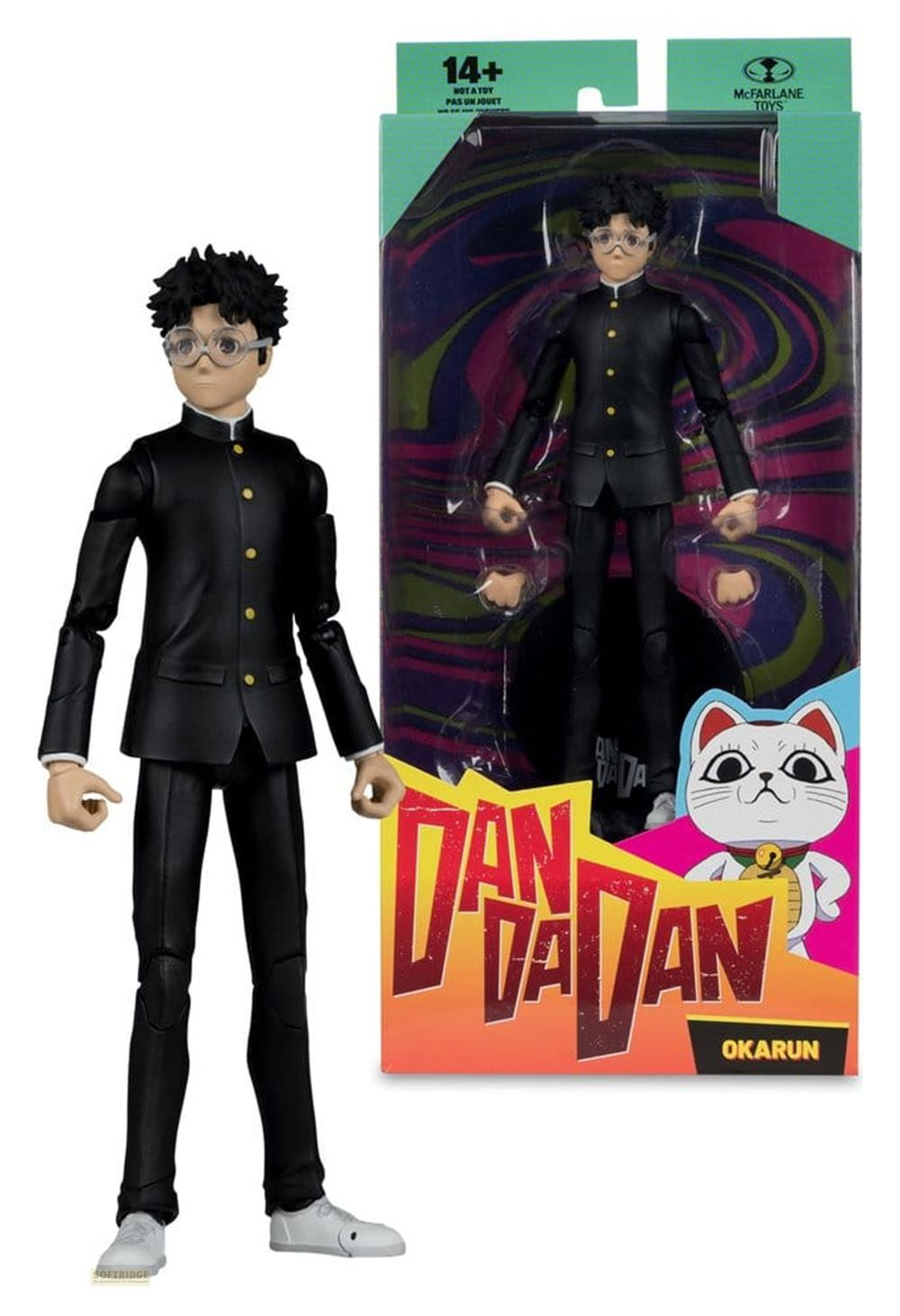 Ein Actionfigur von Okarun in einem schwarzen Anzug steht neben seiner Verpackung.