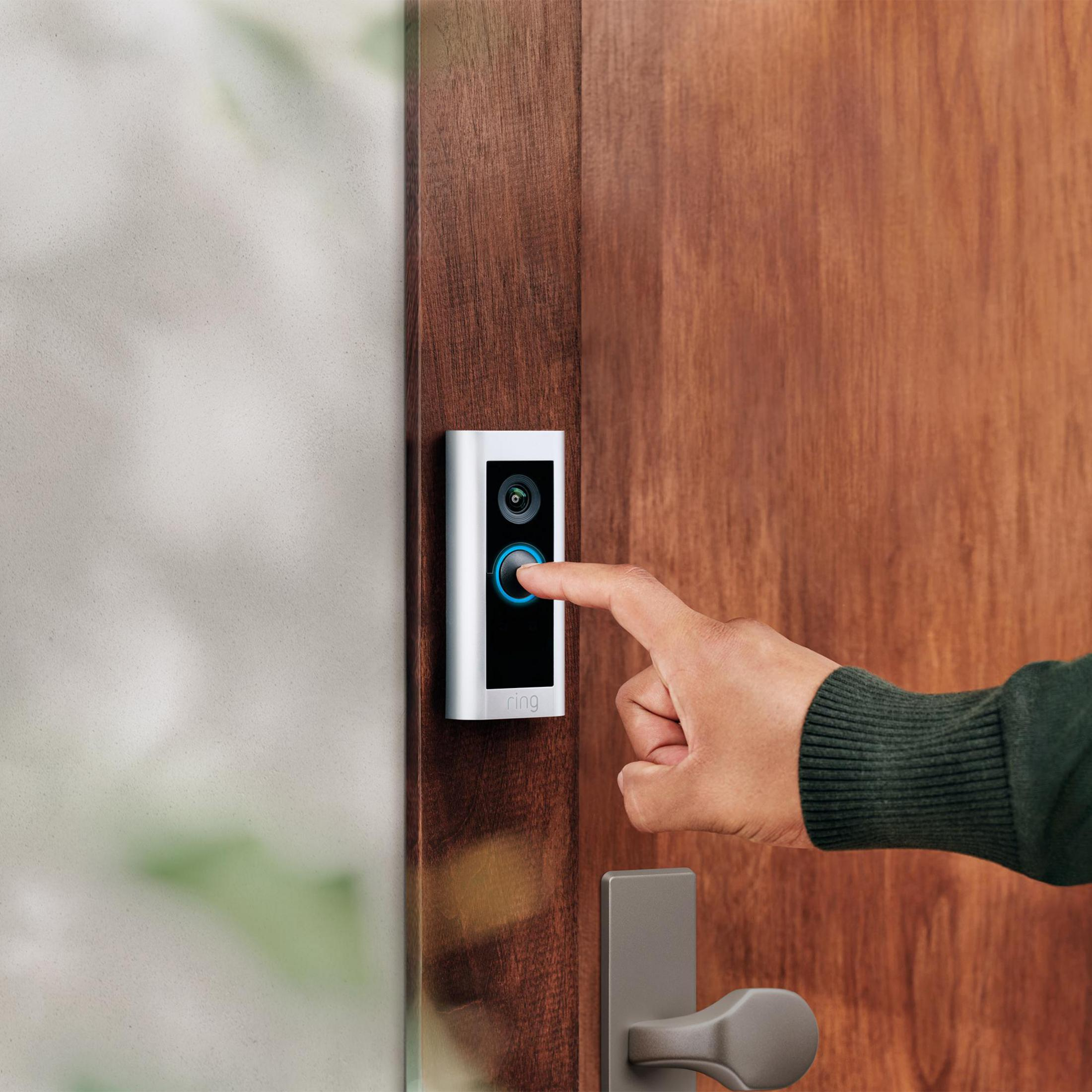 Un dito preme un campanello d'argento con telecamera su una porta di legno.