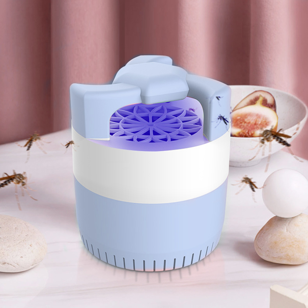 Eine hellblaue und weiße Mückenfalle mit einem violett leuchtenden Gitter, umgeben von Mücken, Feigen und Dekorationssteinen.