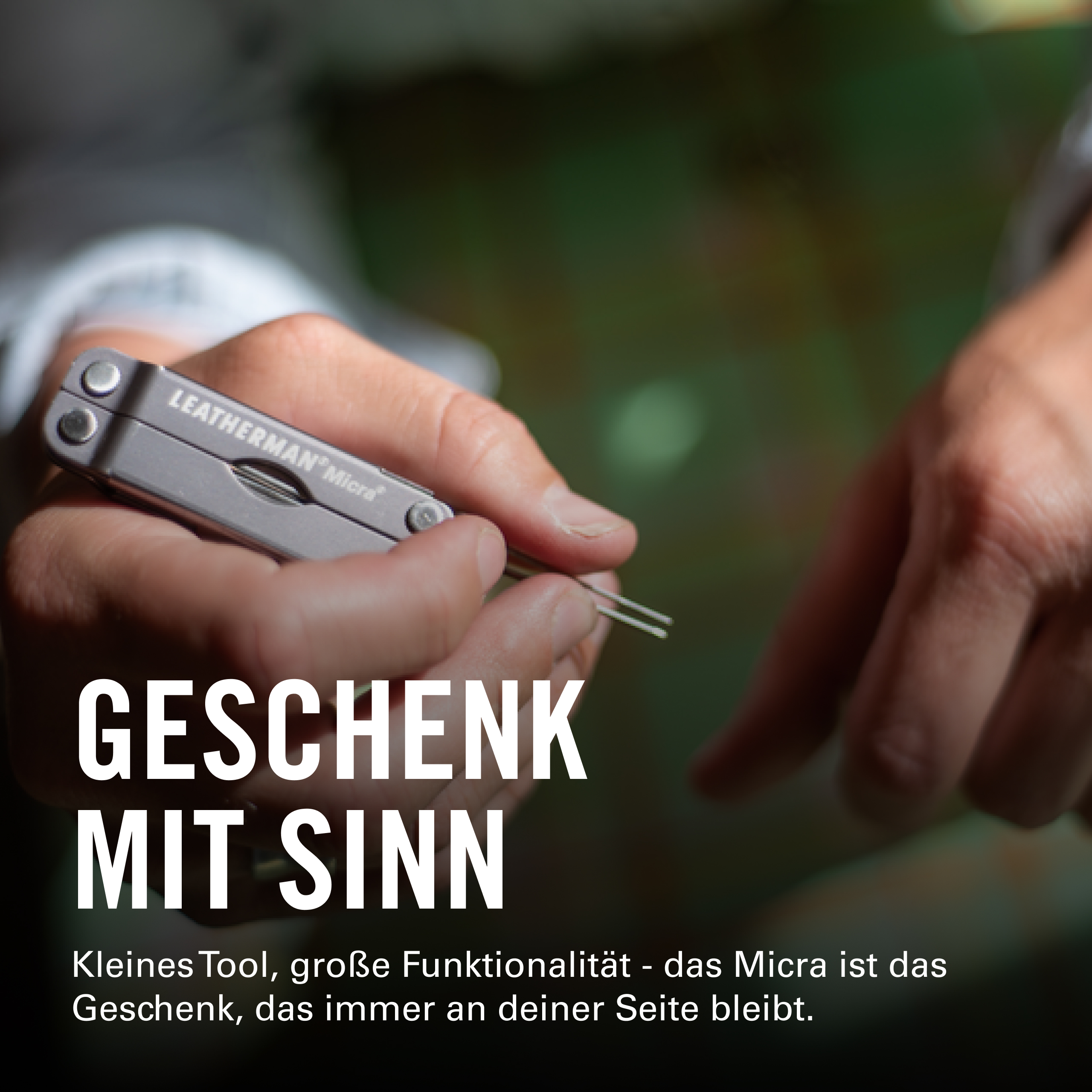 Die Hände einer Person halten ein silbernes Leatherman Micra Multitool mit ausgefahrenen Pinzetten vor einem verschwommenen grünen Hintergrund.
