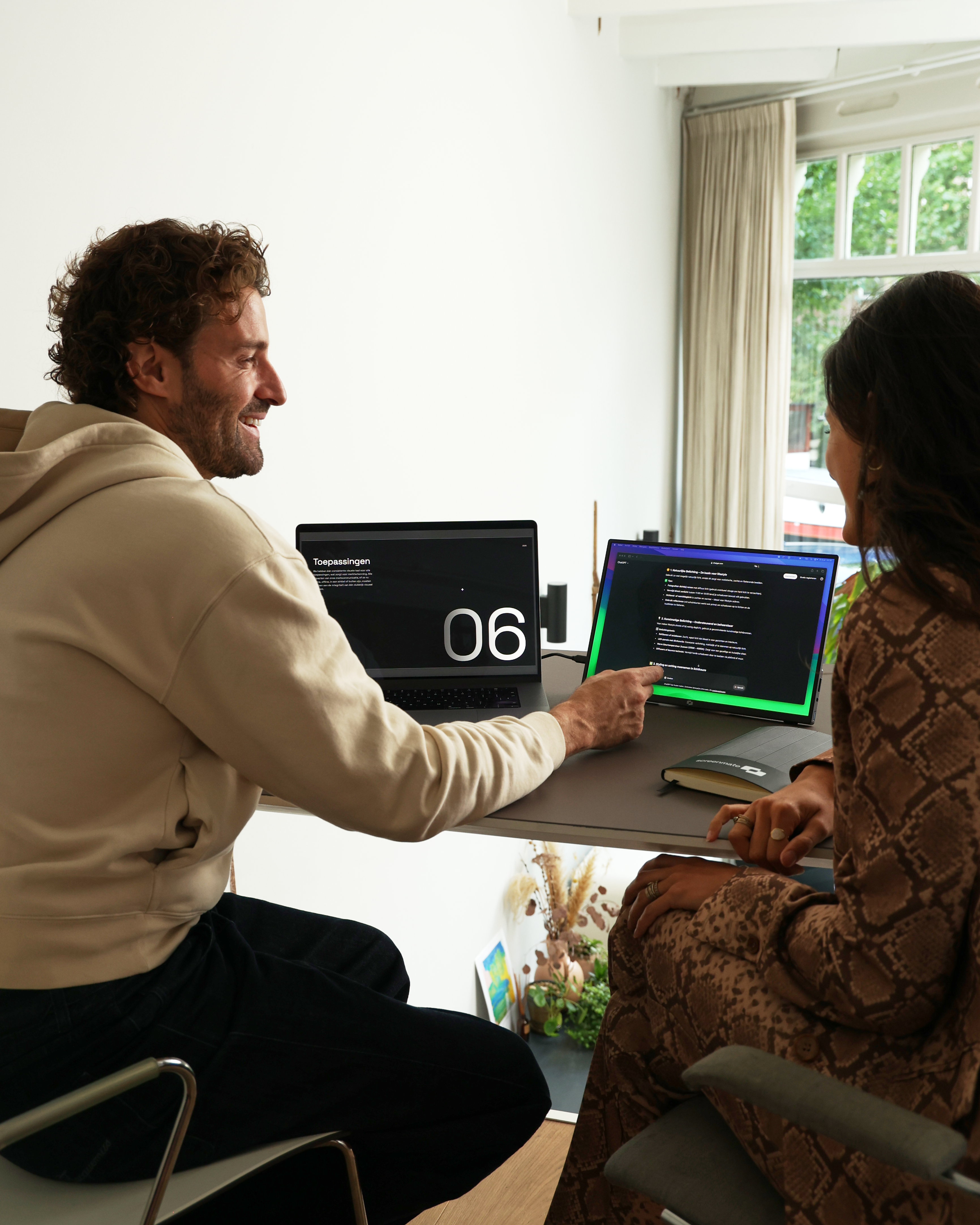 Man en vrouw zitten aan een bureau naar twee schermen te kijken.