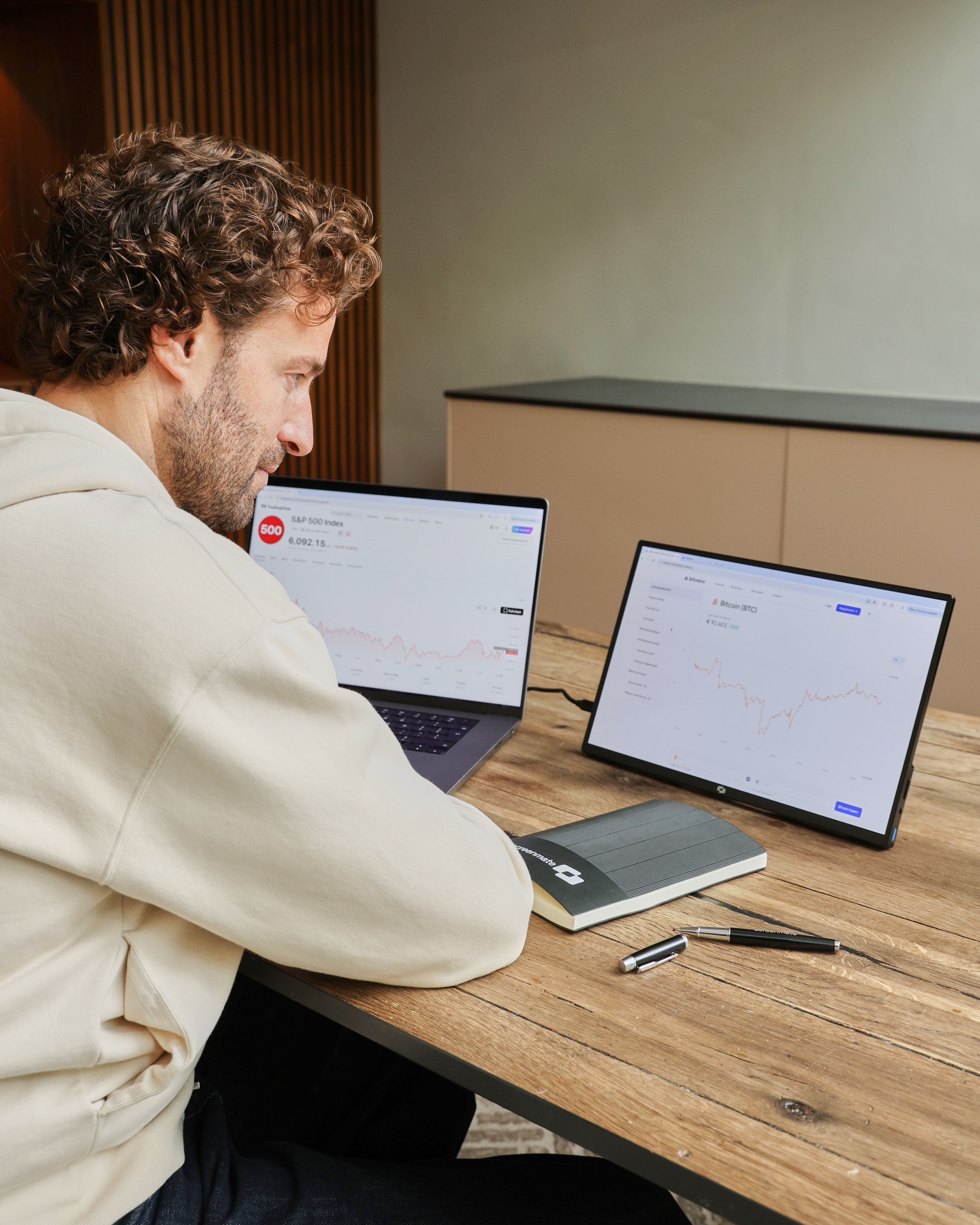 Man aan een bureau met twee monitoren die beursgegevens tonen.