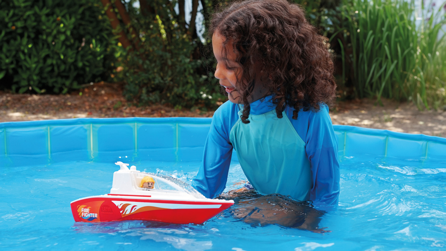 Ein Mädchen spielt mit einem Feuerlöschboot in einem aufblasbaren Pool im Garten.