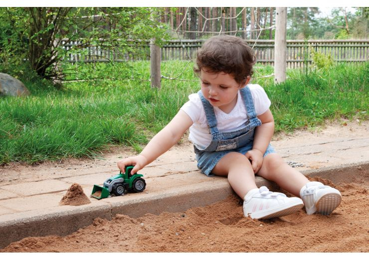 Ein kleines Kind sitzt im Sand und spielt mit einem grünen Spielzeugbagger.