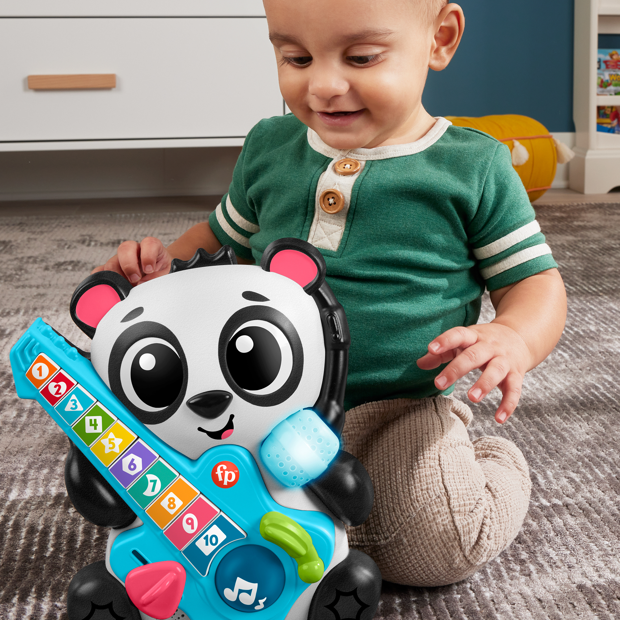 Ein Baby spielt mit einer blauen Panda-Gitarre mit bunten Tasten auf einem Teppich.