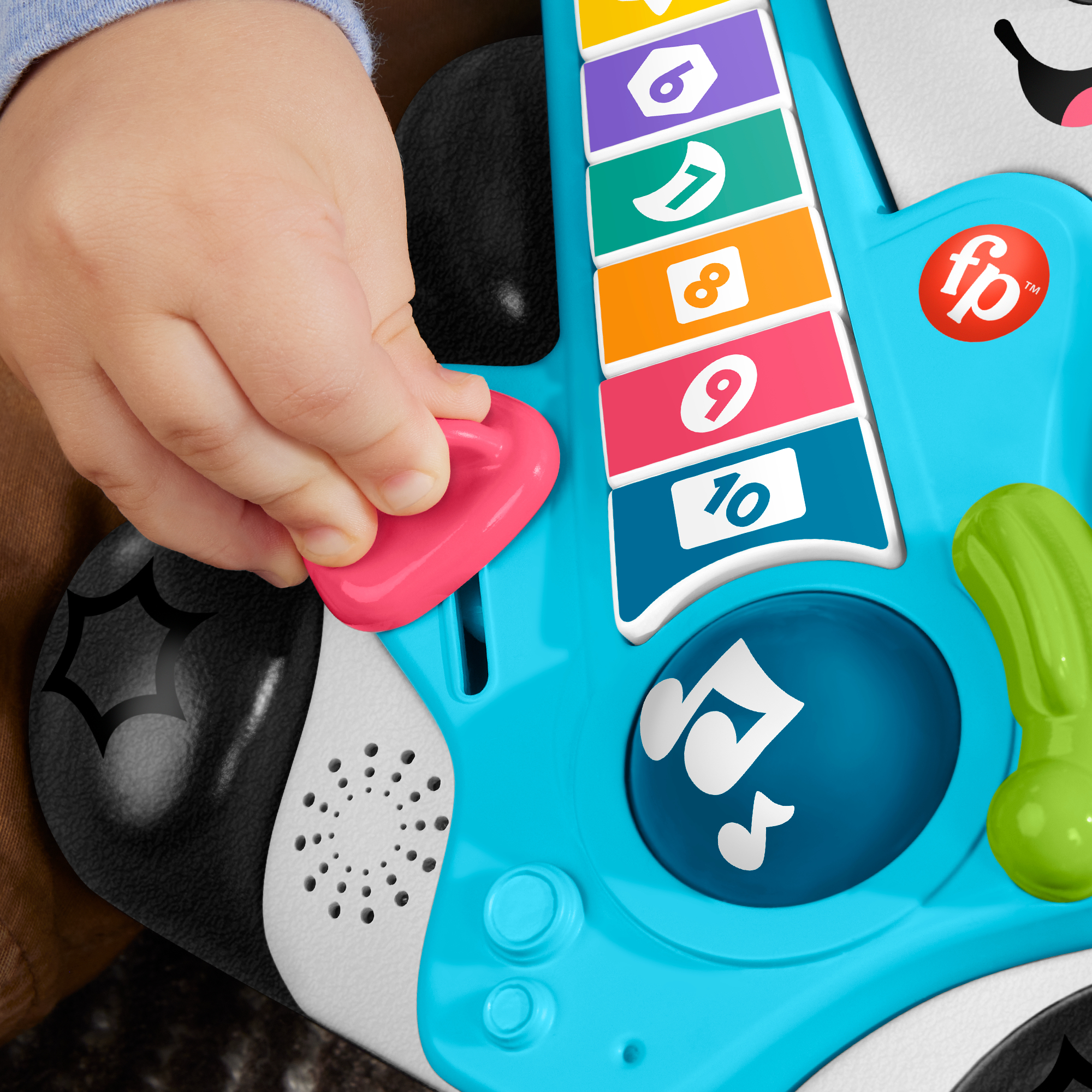 Die Hand eines Kindes drückt einen pinken Knopf an einer blauen Spielzeuggitarre mit bunten Zahlentasten.