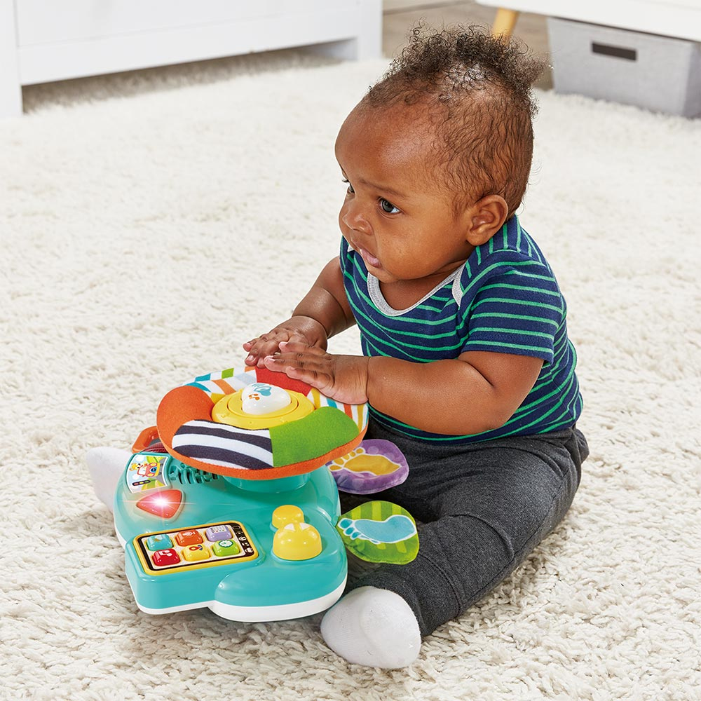 Baby spielt mit einem bunten Spielzeugauto auf einem hellen Teppich.