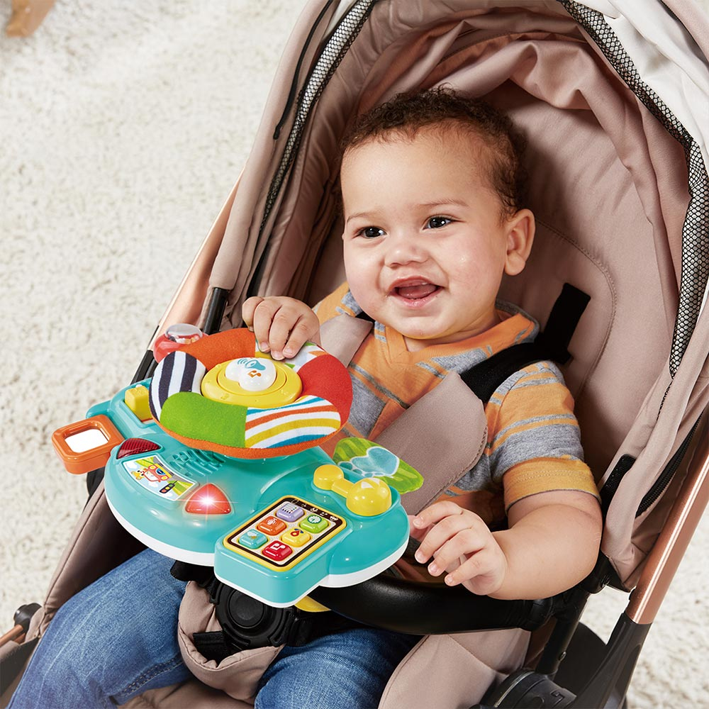 Ein Baby in einem Kinderwagen spielt mit einem bunten Spielzeuglenkrad.