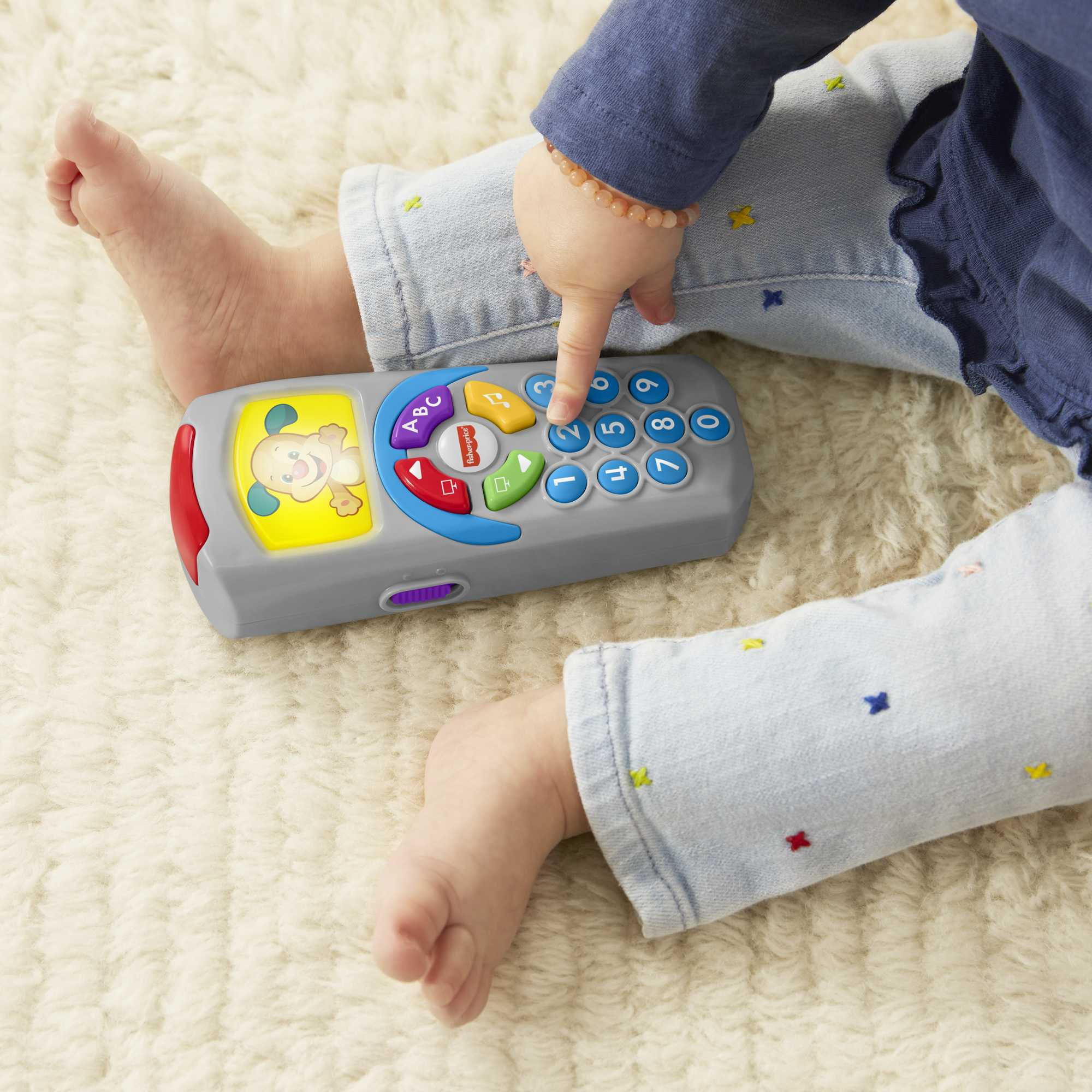 Ein Baby spielt mit einem Spielzeughandy auf einem Teppich.