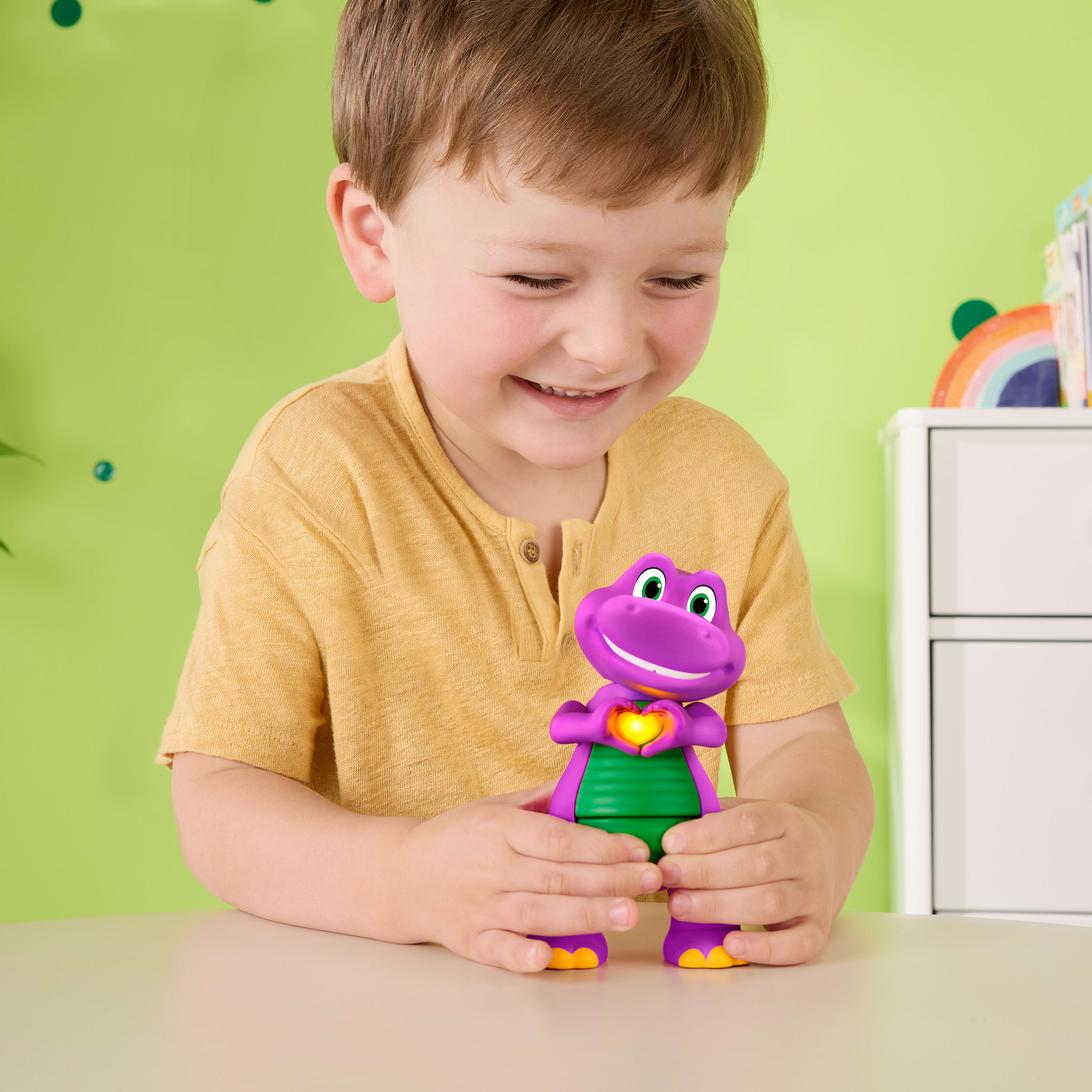 Ein lächelnder Junge im gelben Hemd hält einen lila Spielzeugdinosaurier mit leuchtendem Herzen.